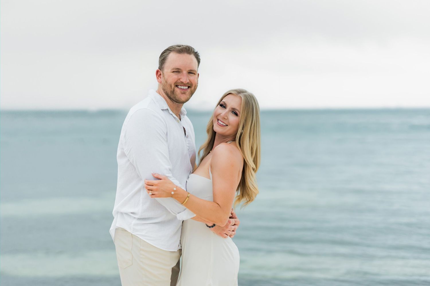 Cancun Engagement Photoshoot - Happy couple embracing on a tropical beach with calm blue ocean waters in the background.