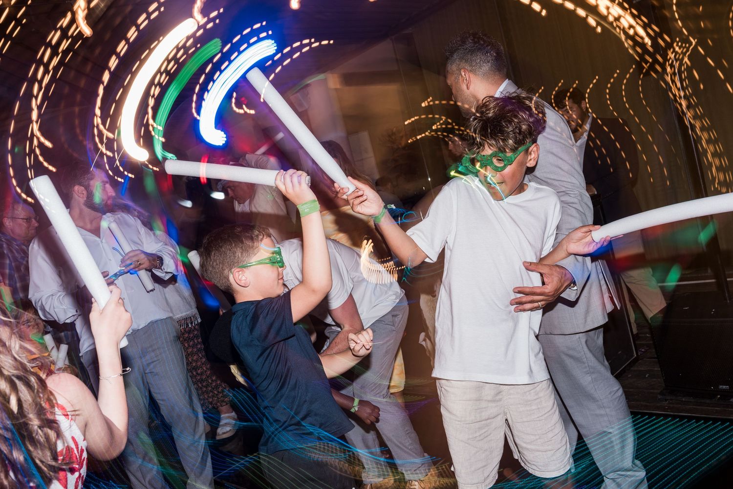 Children dancing with glow sticks at a colorful party celebration with festive lighting effects.