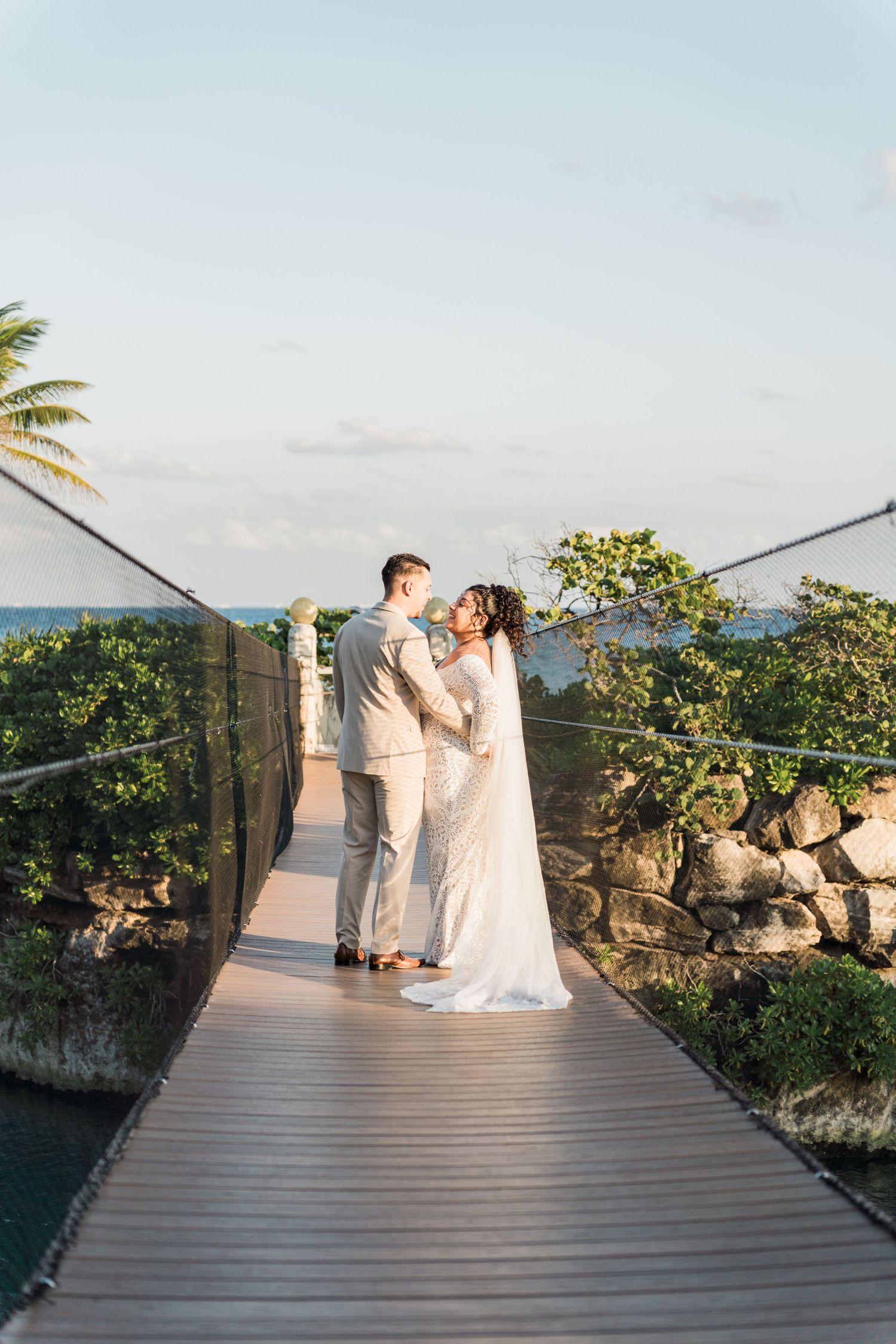 Xcaret Arte Wedding - Bride and groom share a romantic moment on a wooden suspension bridge