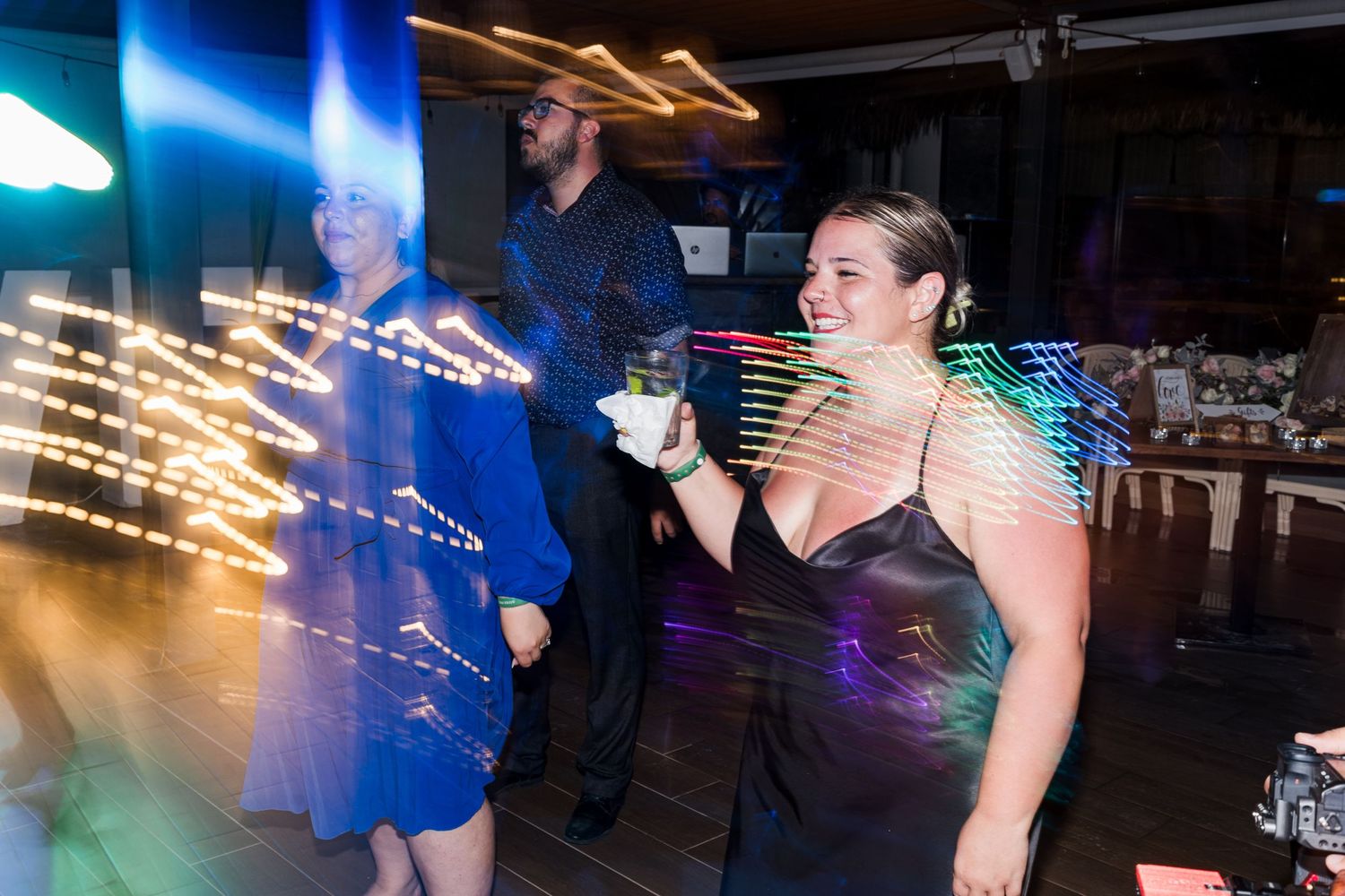 Wedding guests smile and dance joyfully on the reception dance floor with colorful bokeh lights.