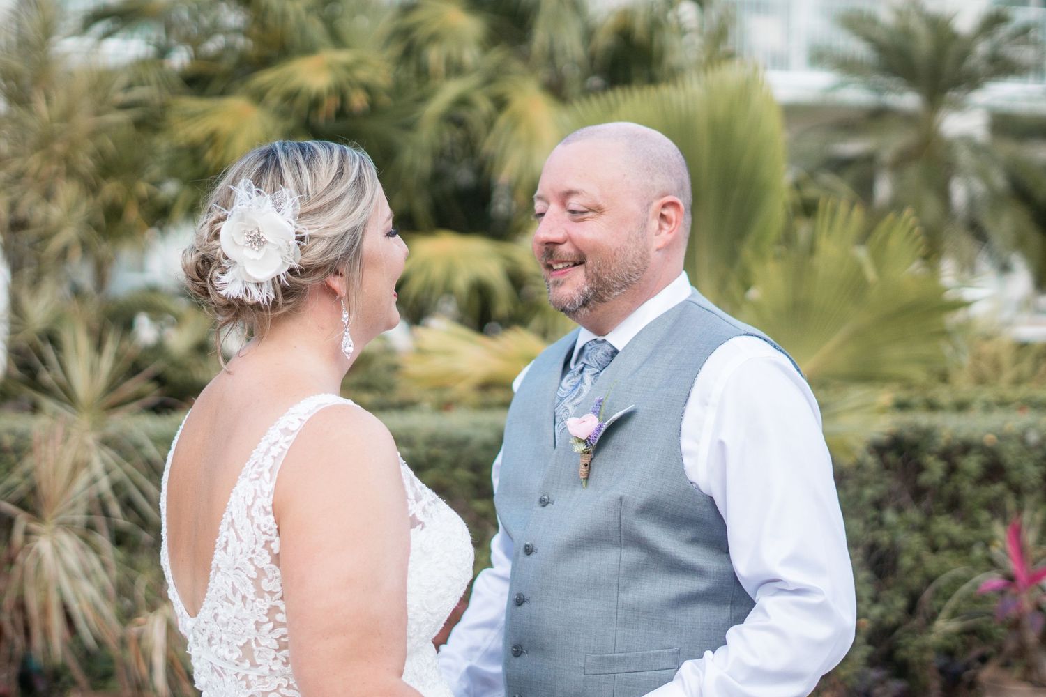 Groom smiles lovingly at bride in lace wedding dress during outdoor portrait session with palms.