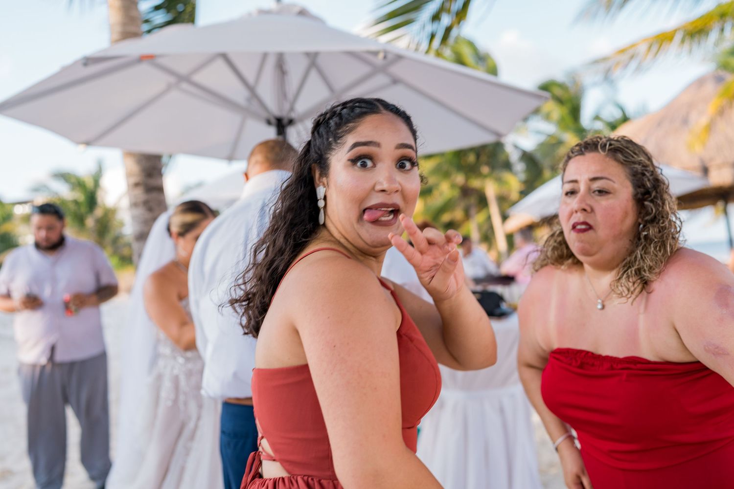 Two women make fun faces and poses together at a lively outdoor beach wedding reception party.