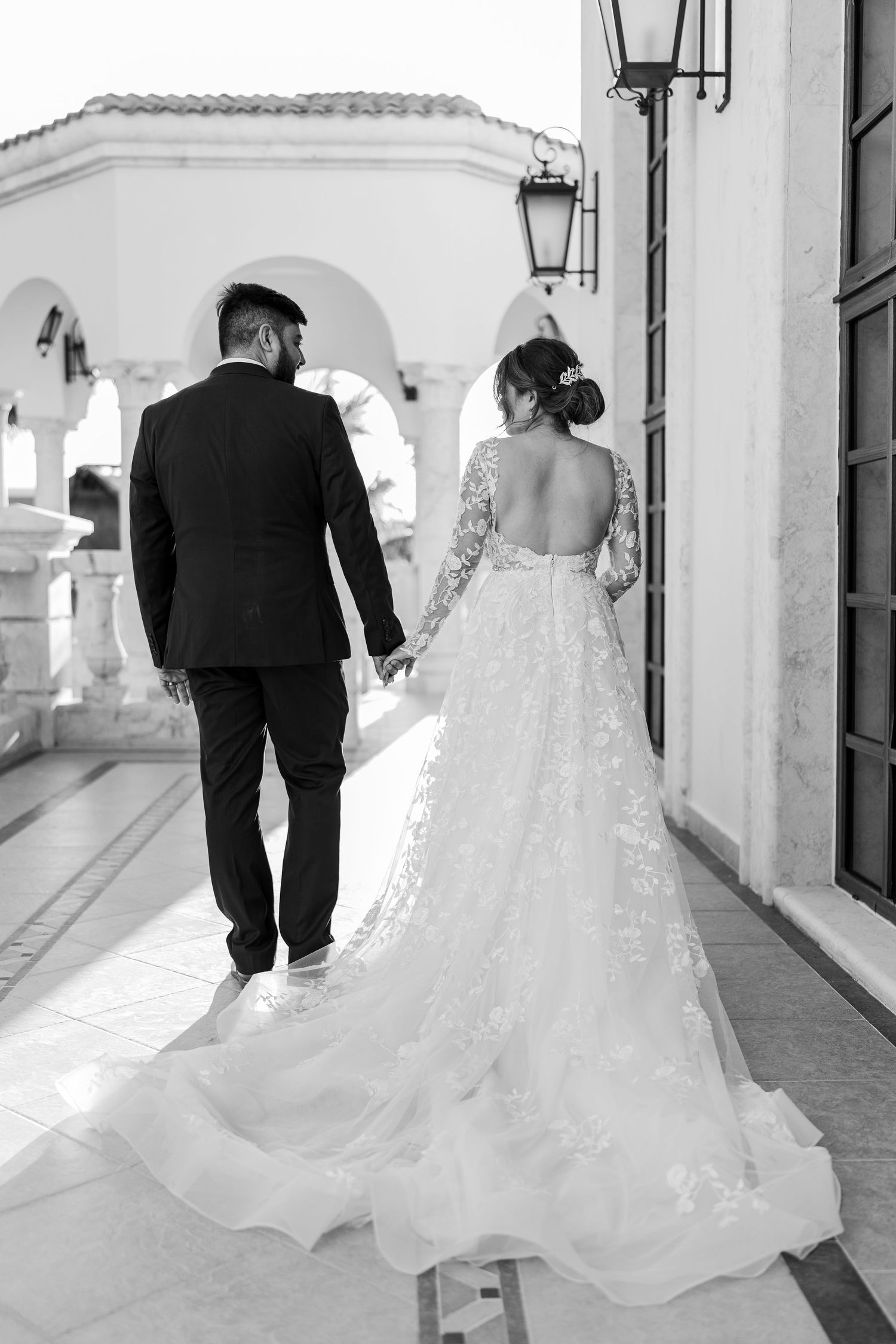 Black and white photo of bride and groom walking hand in hand showing gown train.
