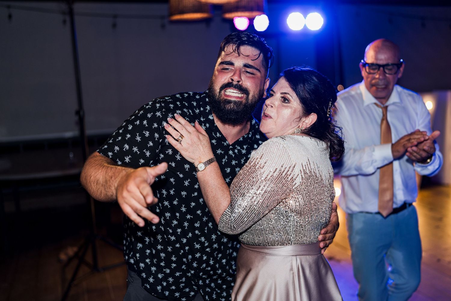 Emotional wedding guests share a warm embrace on the dance floor during reception.