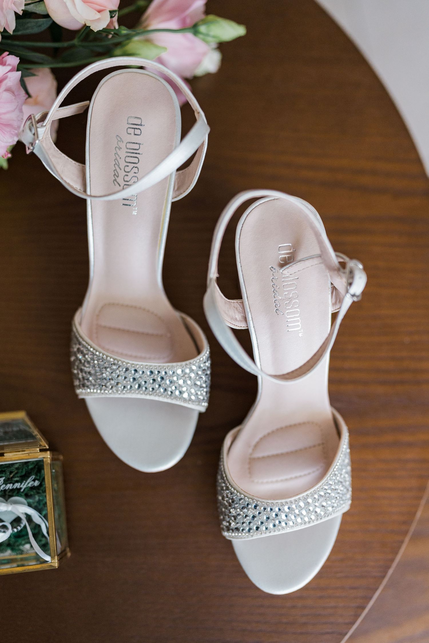 Close-up of elegant crystal-embellished bridal heels by De Blossom on wooden table.
