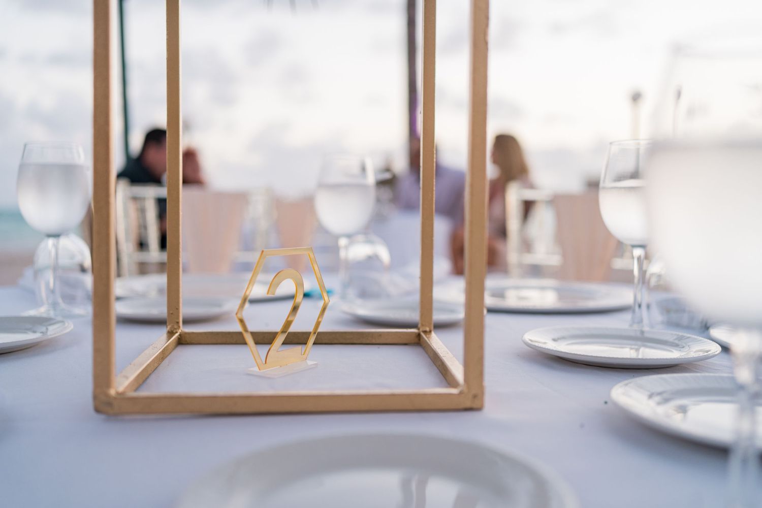 Gold geometric centerpiece on elegant white wedding reception table with glassware.