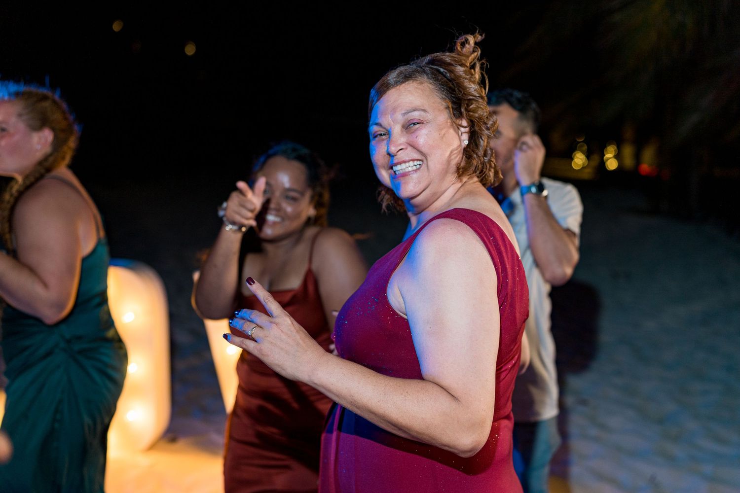 Woman in purple dress smiling and dancing at outdoor beach wedding reception.