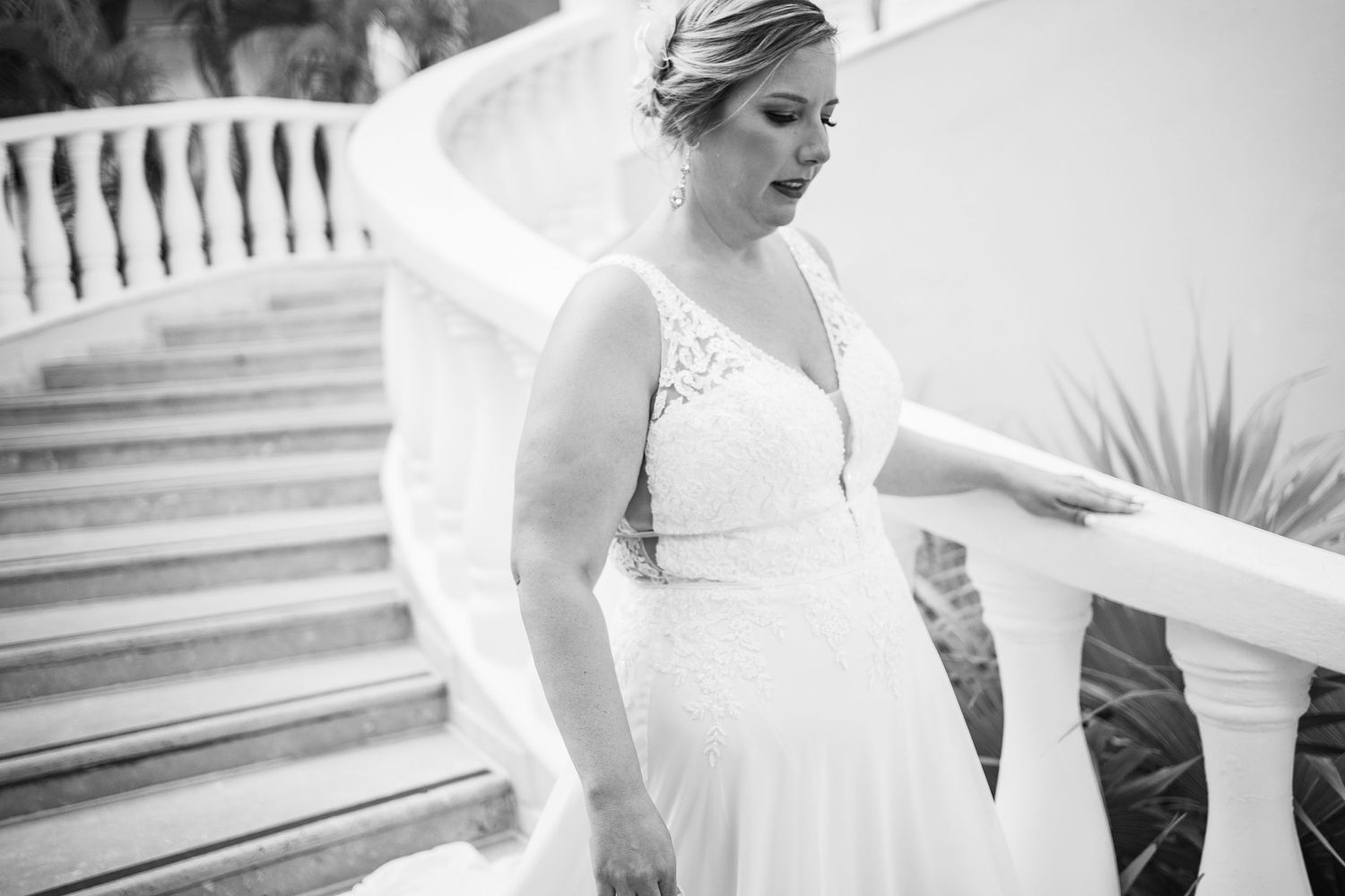 Black and white photo of bride in lace wedding dress descending elegant white spiral staircase.