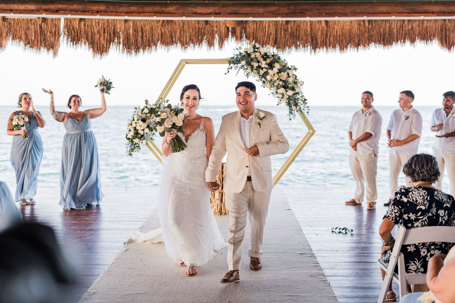 Bride and groom walk down the aisle at a beachfront wedding ceremony with ocean views and floral arch.