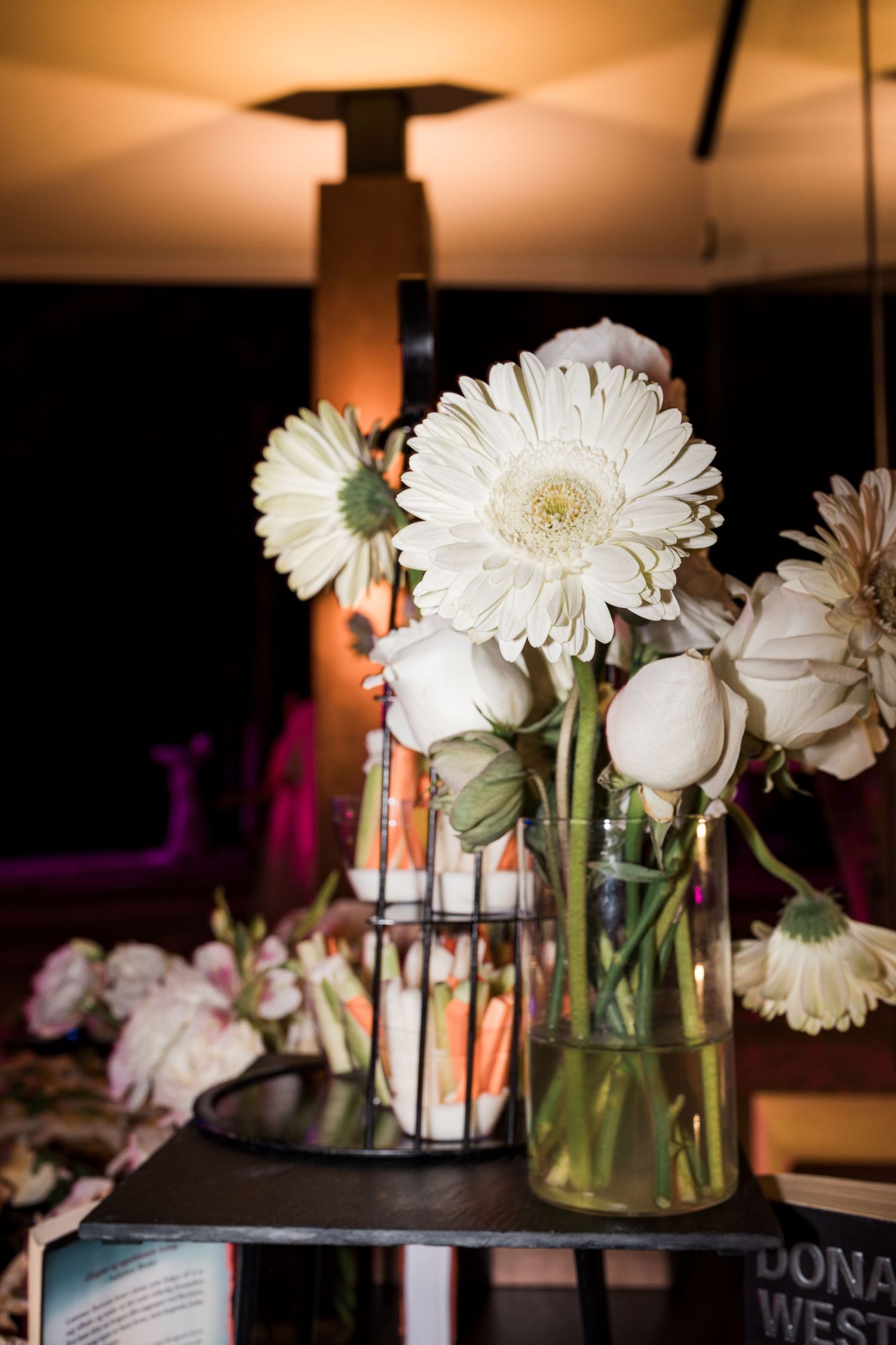 White gerbera daisies and roses arranged in glass vases on a dark table at an elegant event venue.