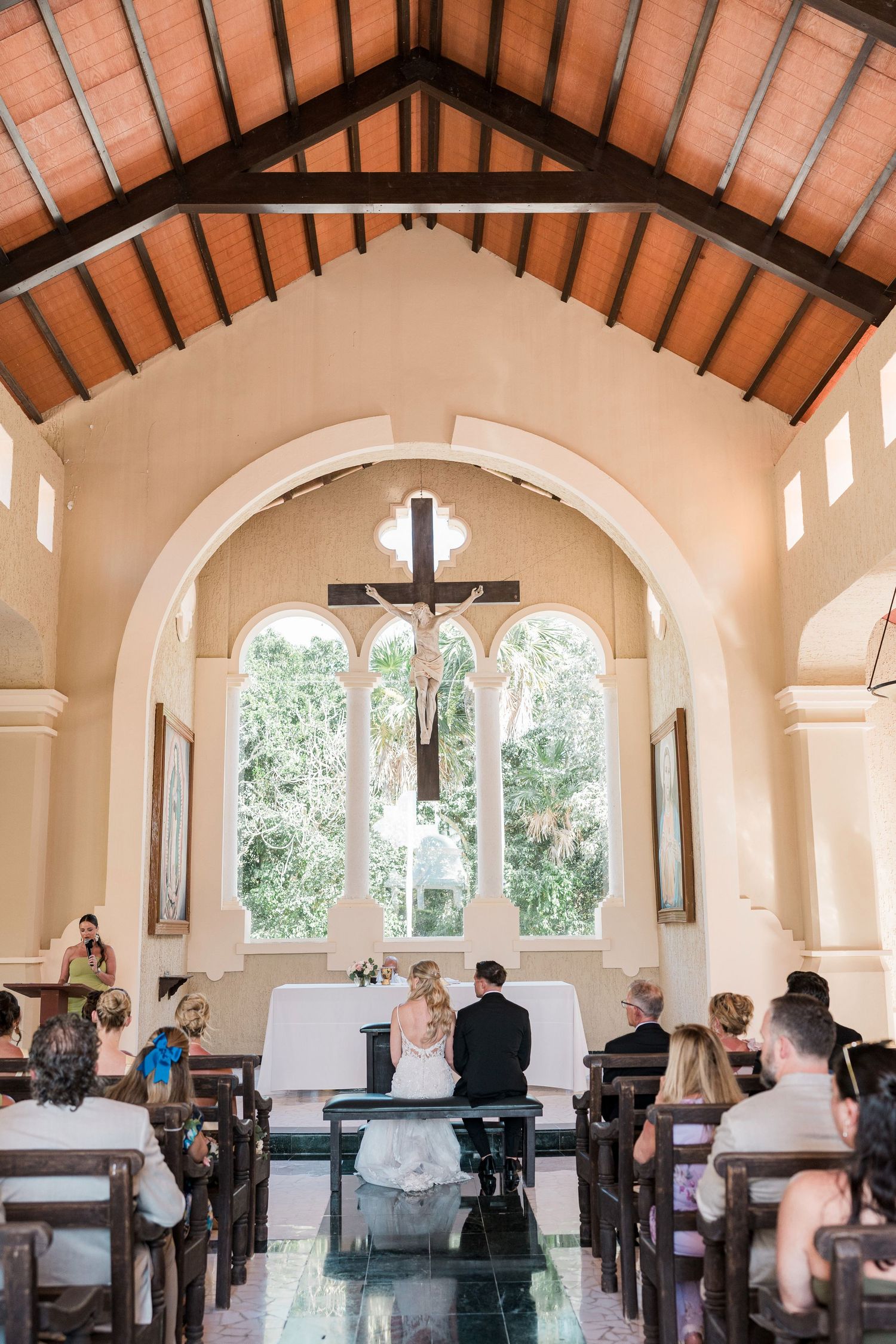 Bride and groom at the altar of a sunlit chapel with wooden ceiling and arched windows during wedding ceremony.