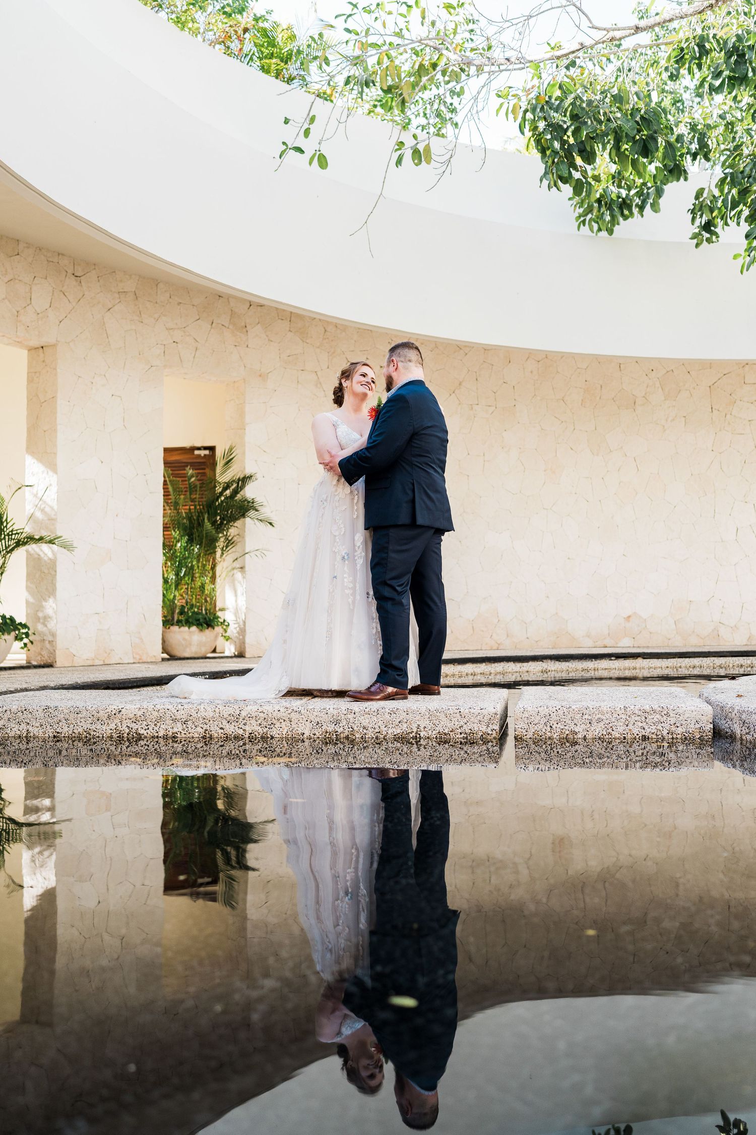 Bride and groom share a romantic moment by a reflective pool in Secrets Akumal Resort.