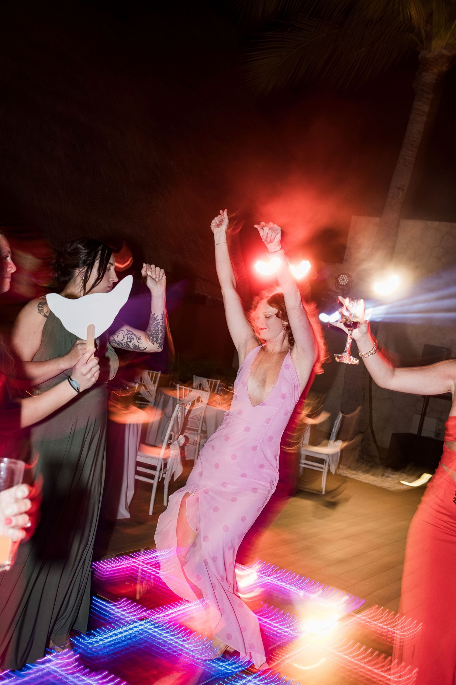 Woman in pink dress dancing energetically at a vibrant night party with colorful LED dance floor and festive lighting.