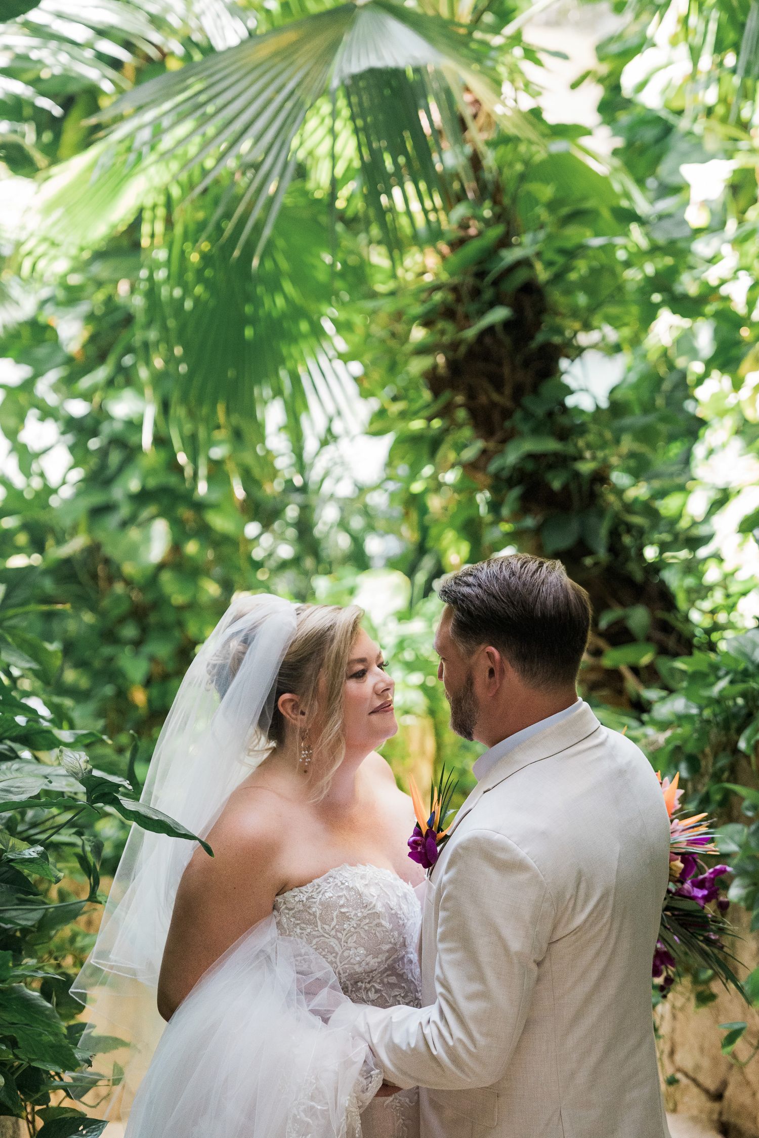 Hotel Xcaret México A bride and groom share an intimate moment surrounded by lush tropical greenery during their outdoor wedding ceremony.