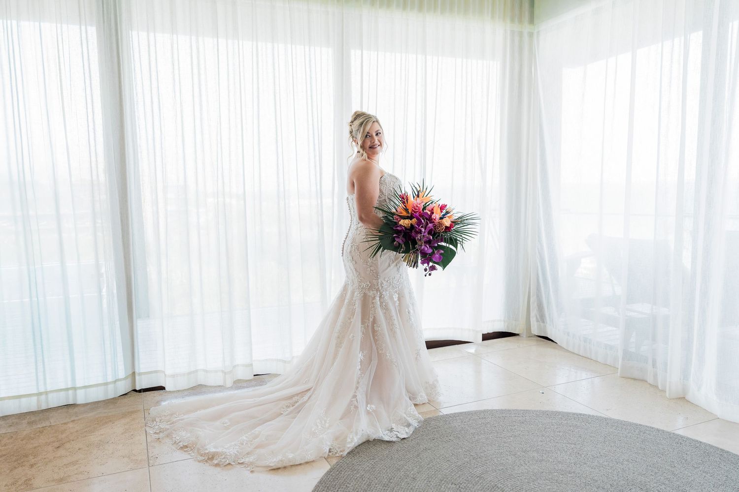 Hotel Xcaret México wedding - Bride in a fitted white lace gown holding a vibrant tropical bouquet
