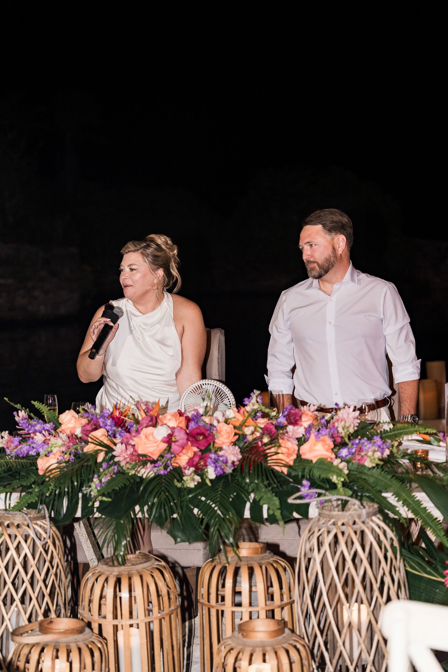 Hotel Xcaret México wedding Bride and groom stand behind a floral centerpiece with tropical flowers and bamboo lanterns