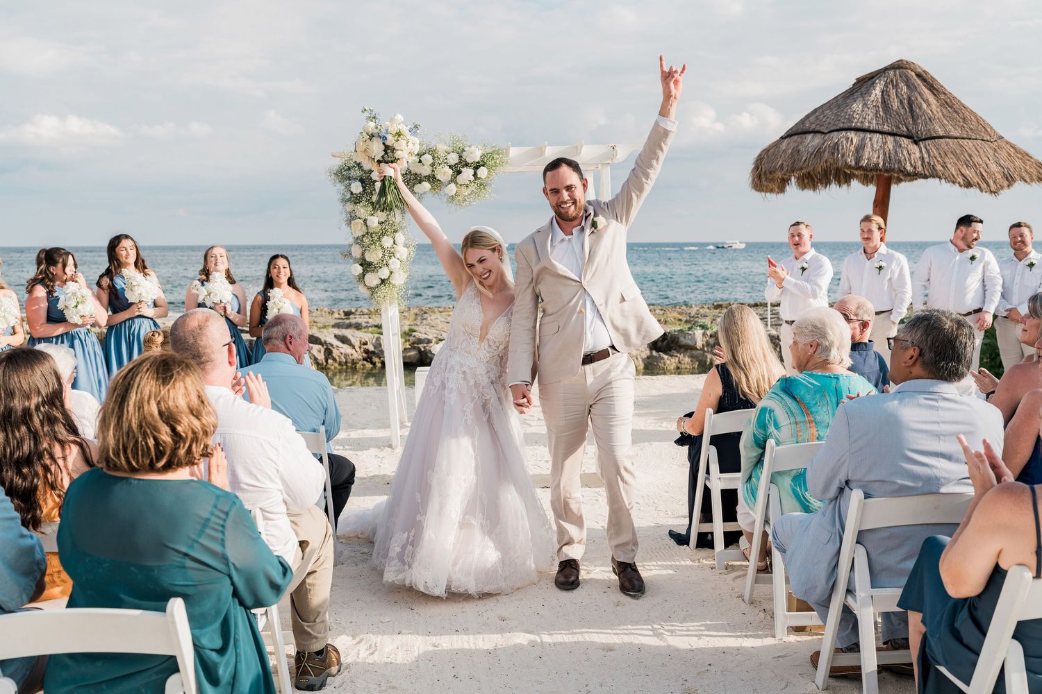 Joyful newlyweds celebrate at outdoor beach wedding ceremony with guests seated. Puerto Vallarta wedding photographer