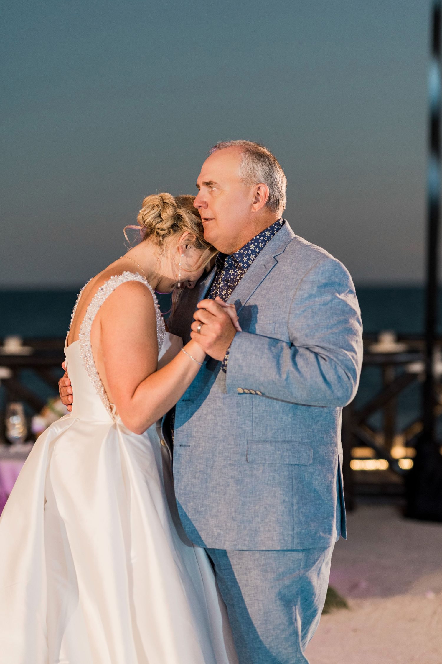 Bride and father share an emotional first dance at a beachside wedding reception at sunset.