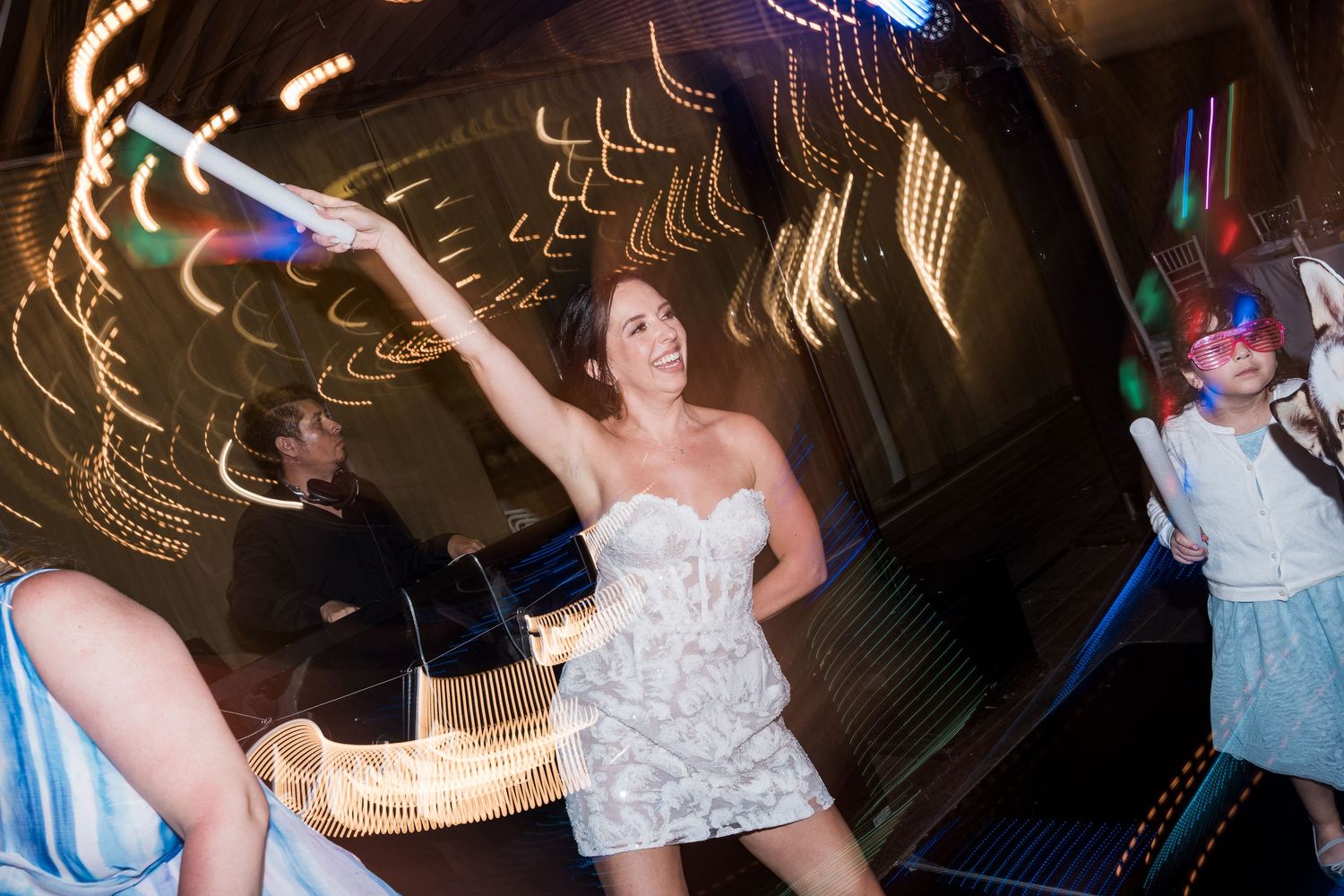 Woman in white dress dancing with light wand at a party with colorful bokeh lights in background.