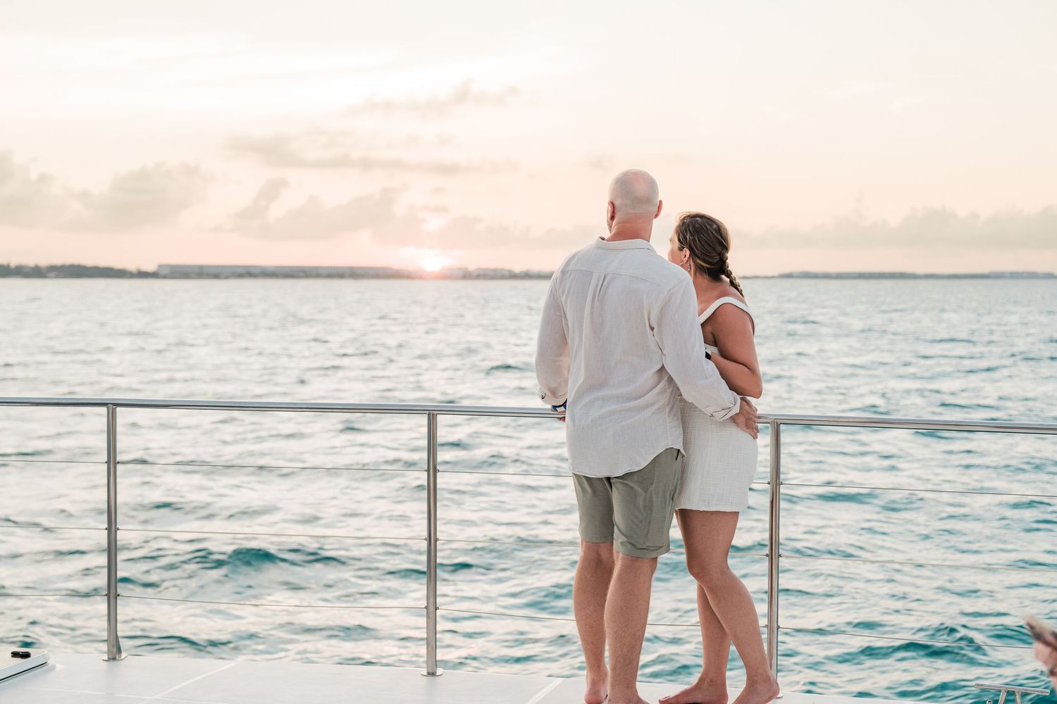 Couple embracing at sunset on a yacht deck overlooking calm turquoise ocean waters.