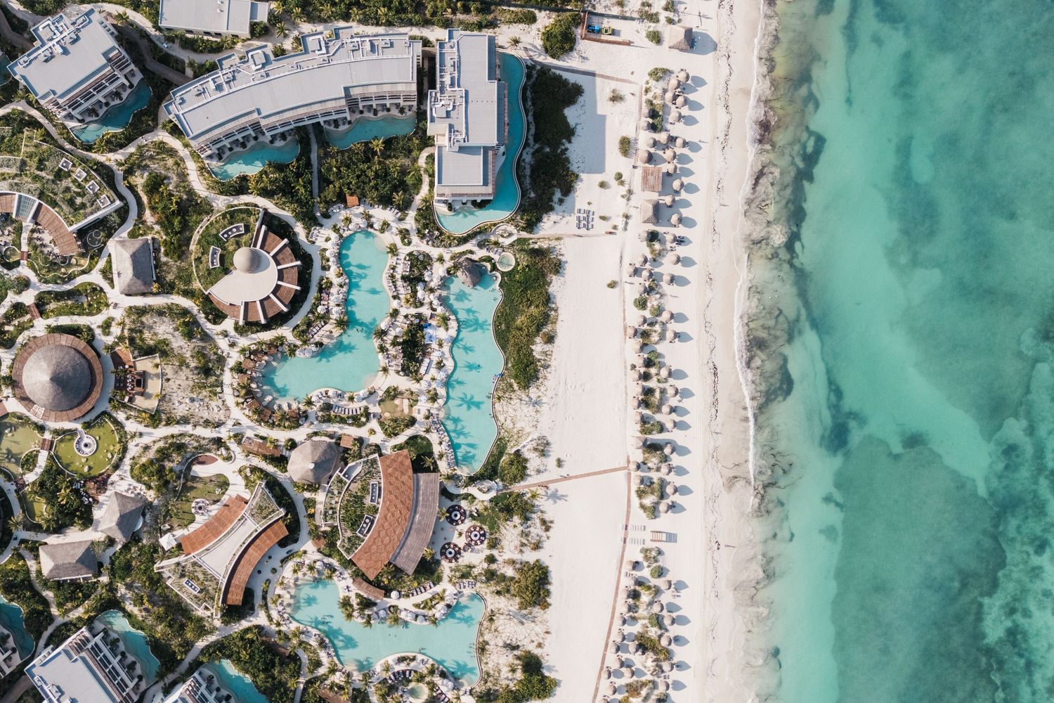 Aerial view of a luxury beachfront resort with turquoise pools, lush gardens, and white sandy beach along crystal-clear Caribbean waters.