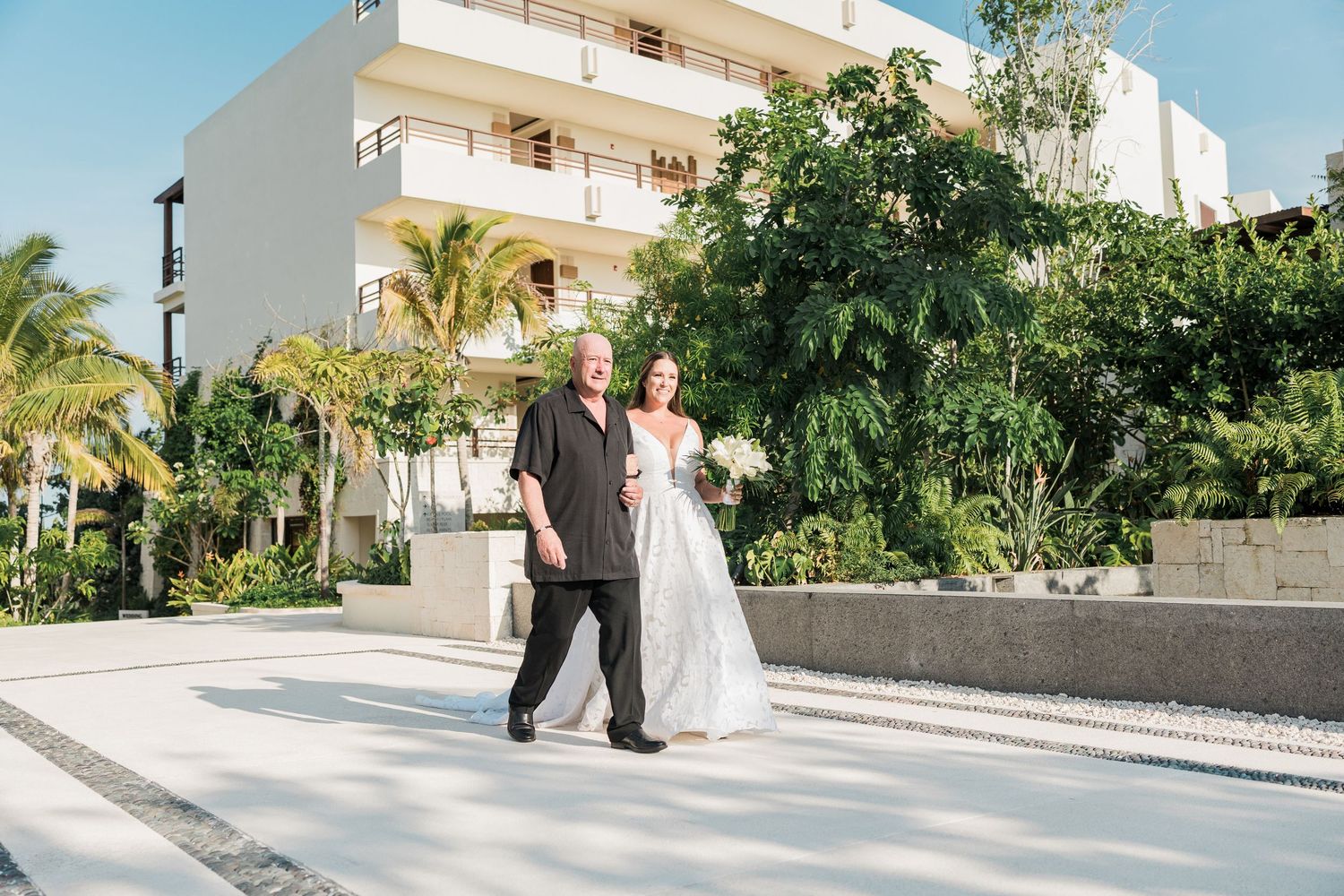 Bride and groom walking together outdoors at a tropical resort wedding venue with lush greenery.