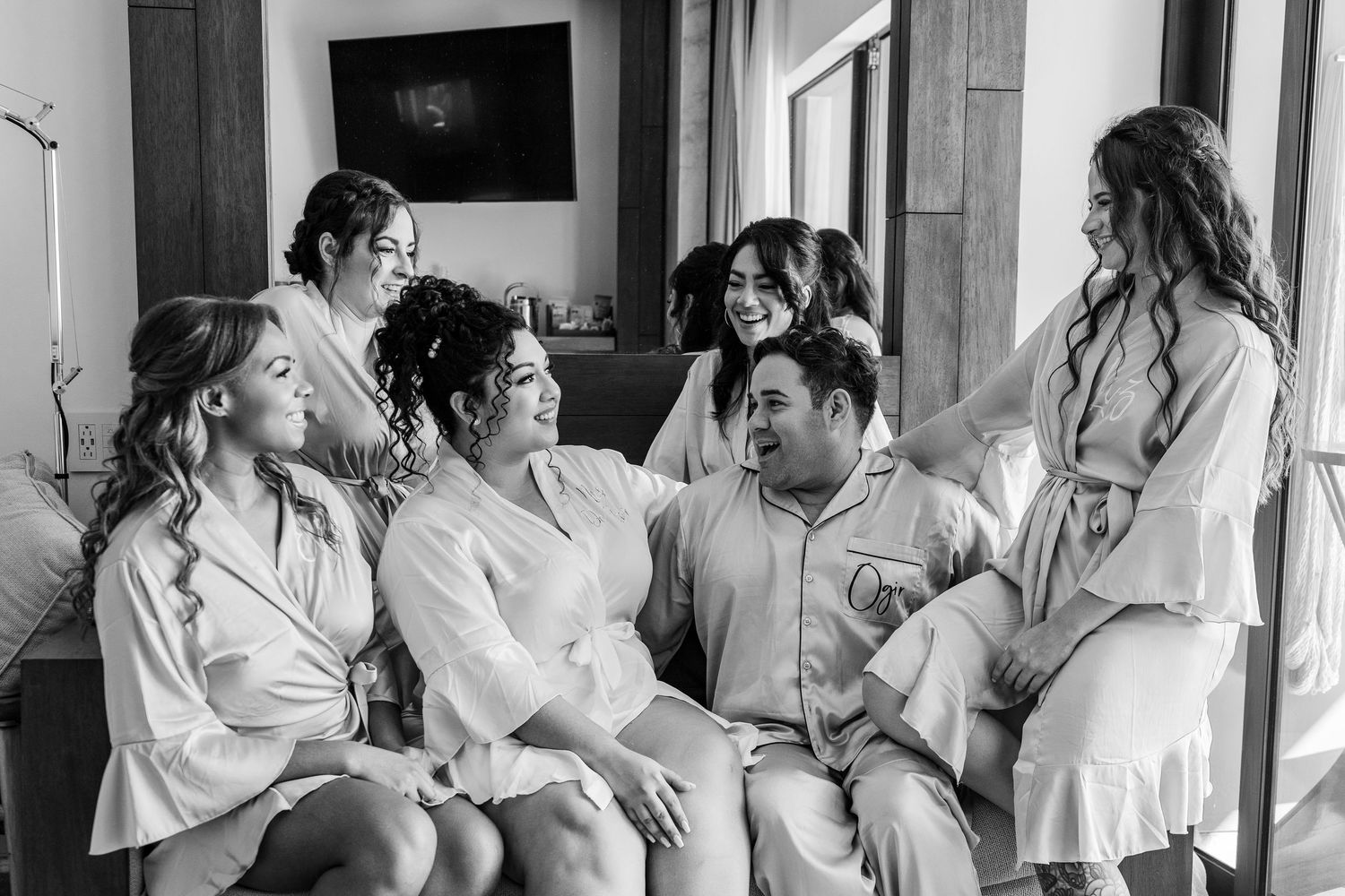 Xcaret Arte Wedding - Black and white photo of a bride, groom, and bridesmaids laughing together in robes during wedding preparations.