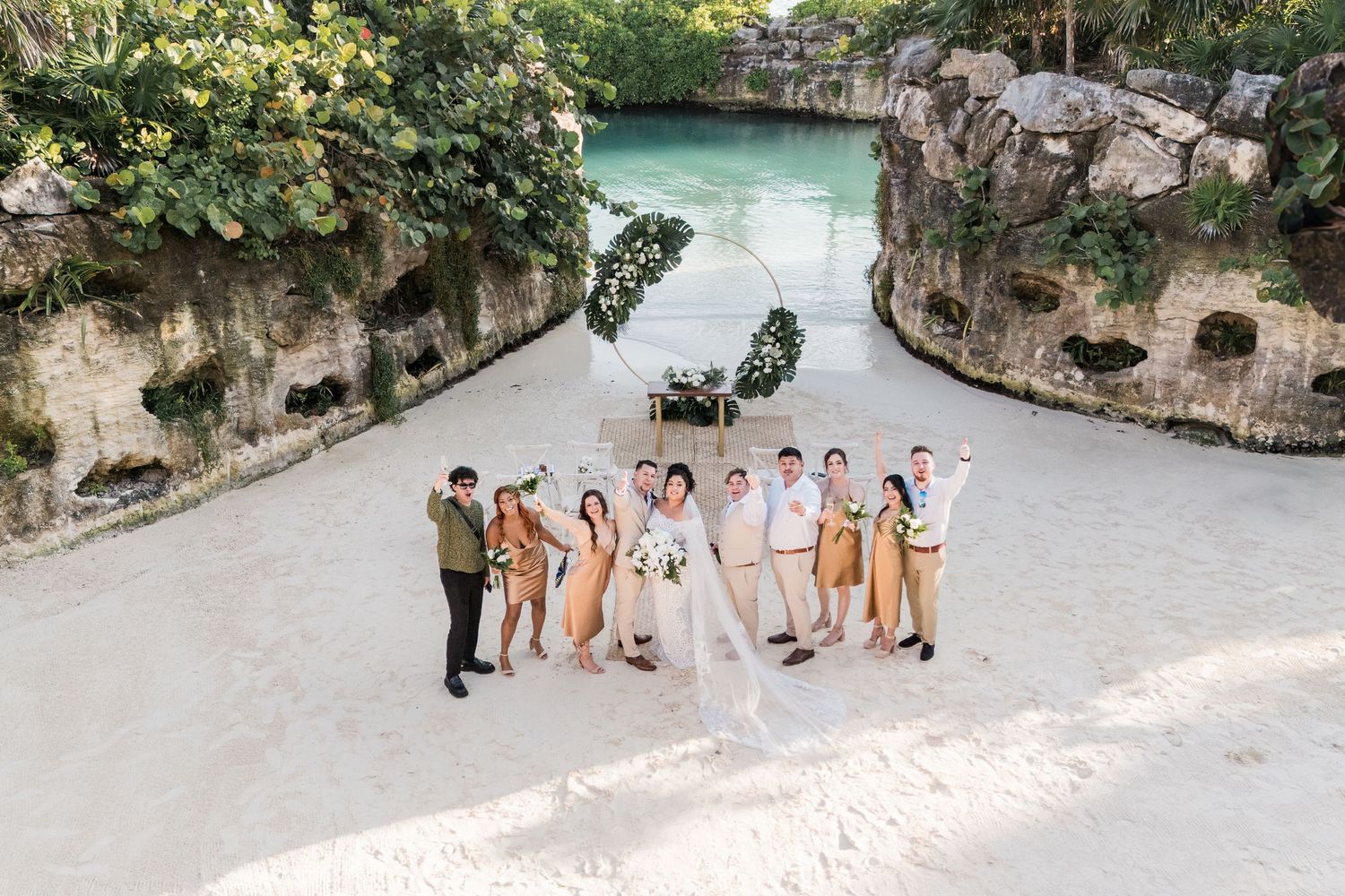 Xcaret Arte Wedding - Wedding party celebrates on a white sand beach with turquoise water and stone cliffs in a tropical paradise.