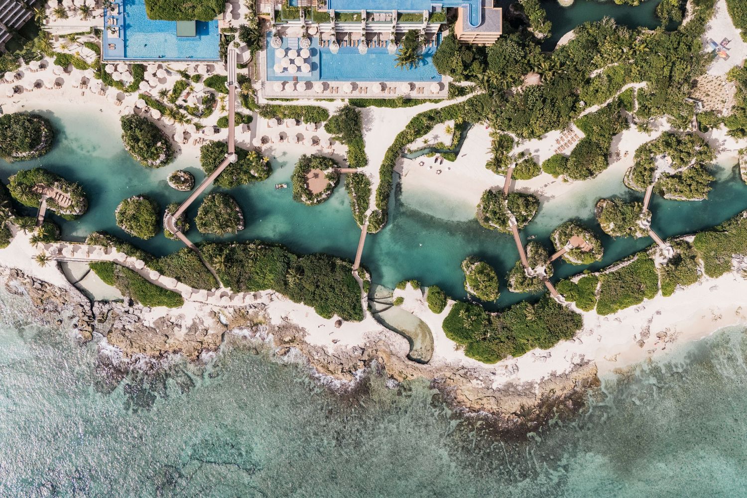 Xcaret Arte WedAerial view of a luxury tropical resort with winding lagoons, lush greenery, and turquoise waters along a pristine coastline.