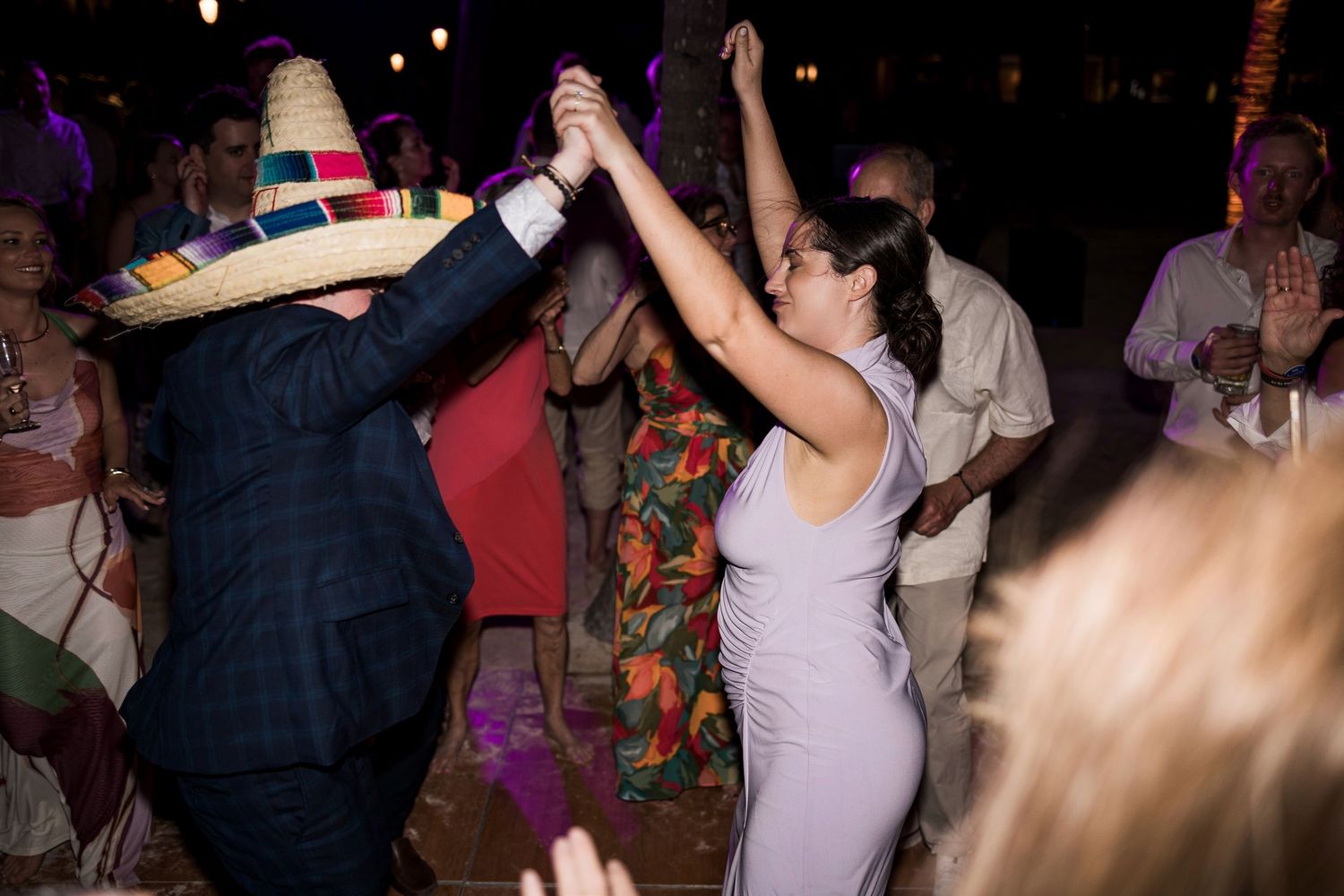 Couple dancing at a festive wedding reception, one partner wearing a colorful sombrero hat on the dance floor.