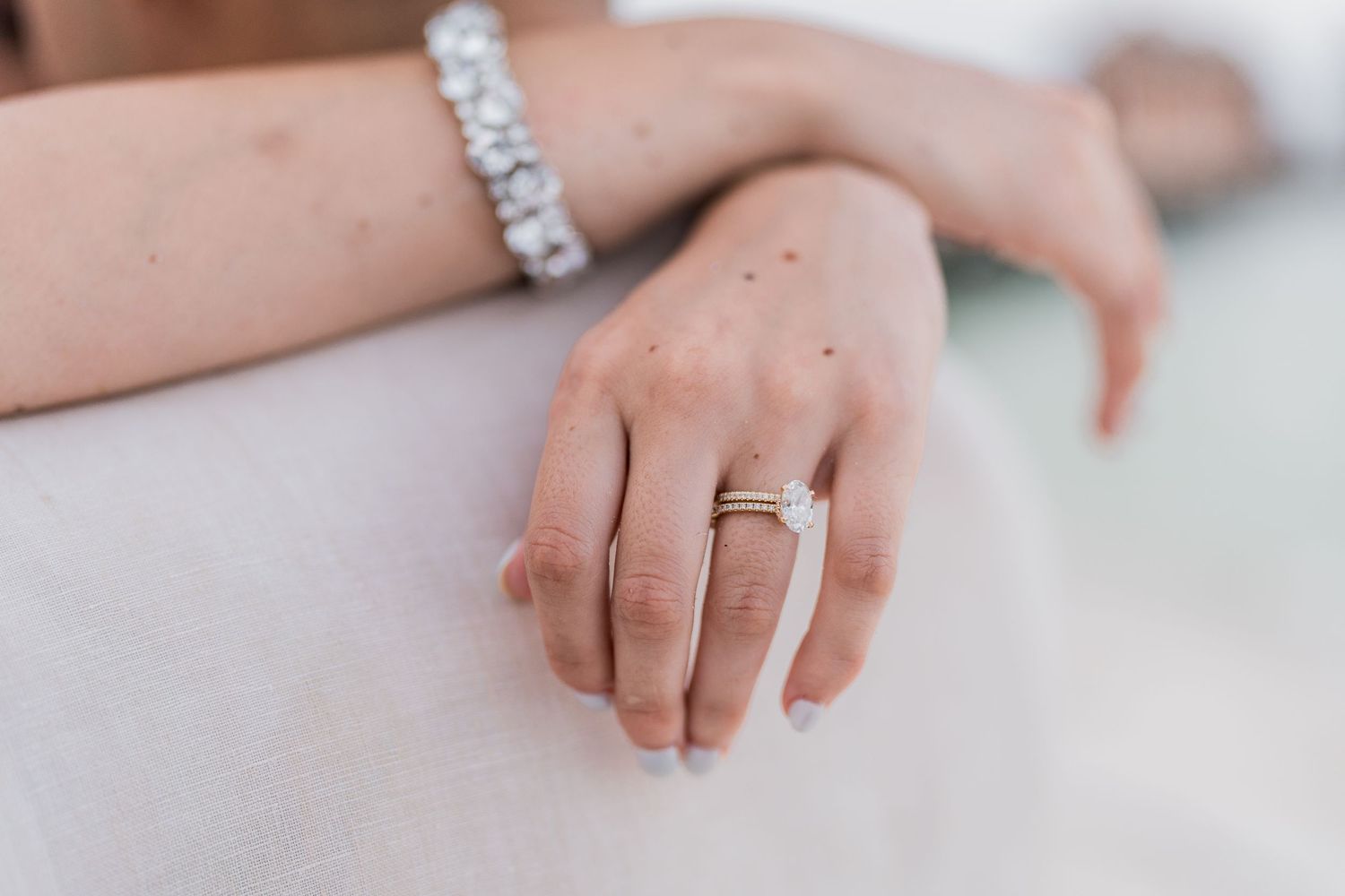 Close-up of a bride's hand showcasing a diamond engagement ring and elegant bracelet on white fabric.