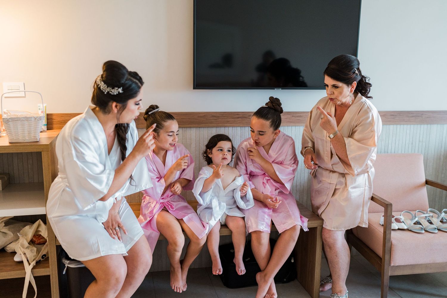 Bride and bridesmaids in robes sitting together with young flower girls before the wedding.