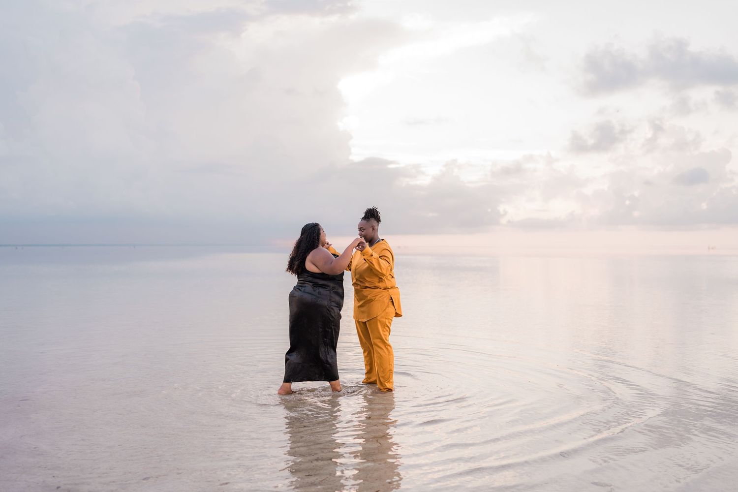 Two women standing together in shallow ocean water at dusk.