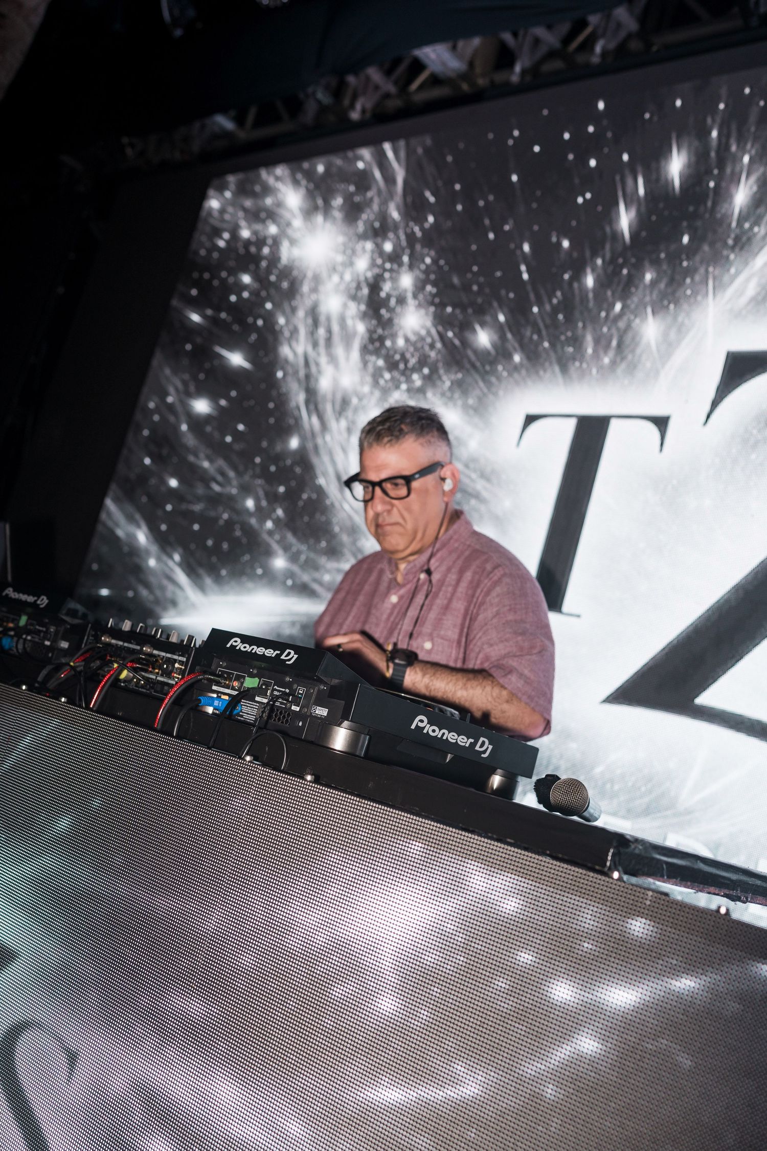 A DJ performs behind Pioneer DJ equipment at a nightclub with a dramatic starry projection backdrop.