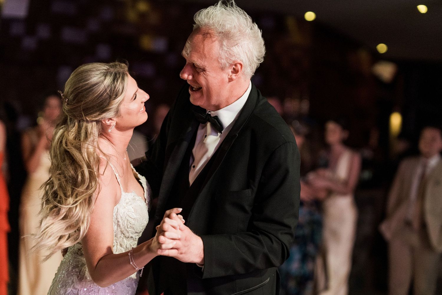 Bride and older gentleman share a first dance at a wedding reception in elegant formal attire.