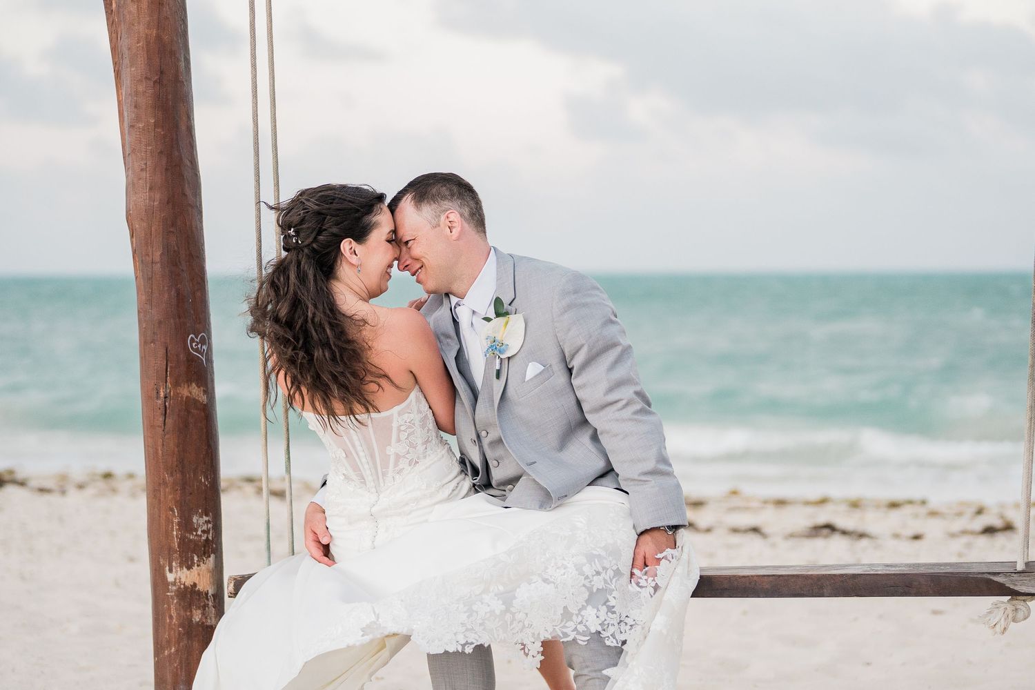 Bride and groom sharing a romantic kiss on a beach swing at grand palladium costa mujeres