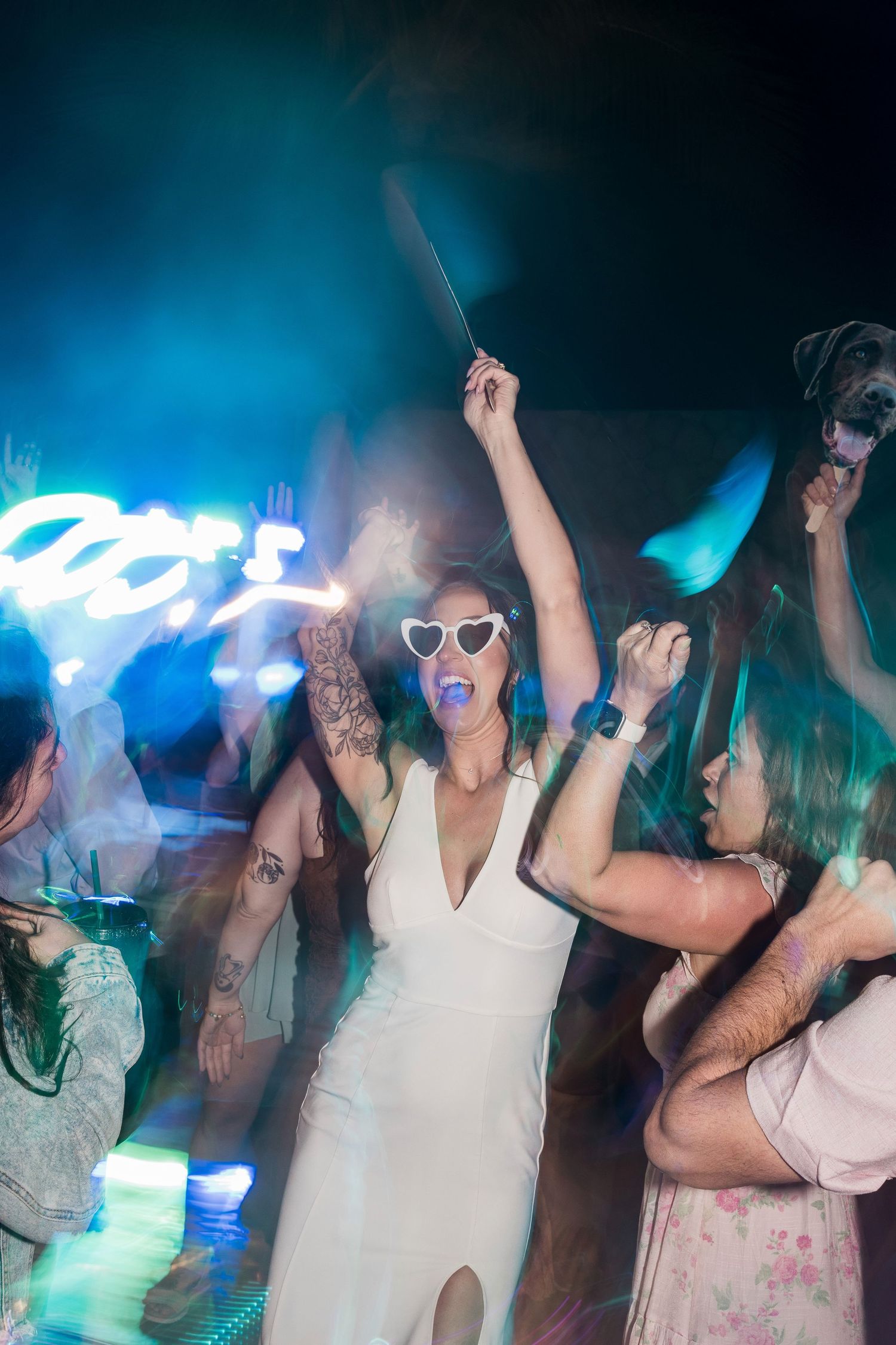 Bride in white dress and heart sunglasses dancing with sparkler at wedding reception party.