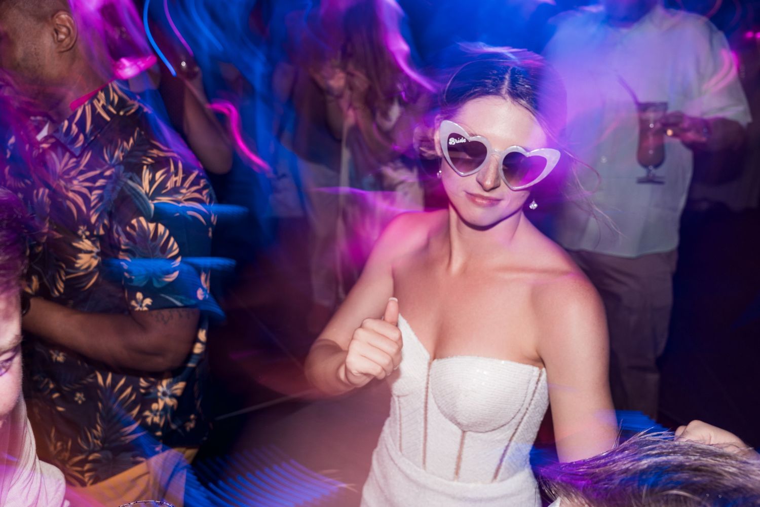 Woman in white strapless dress and heart-shaped sunglasses dancing at a nightclub party.