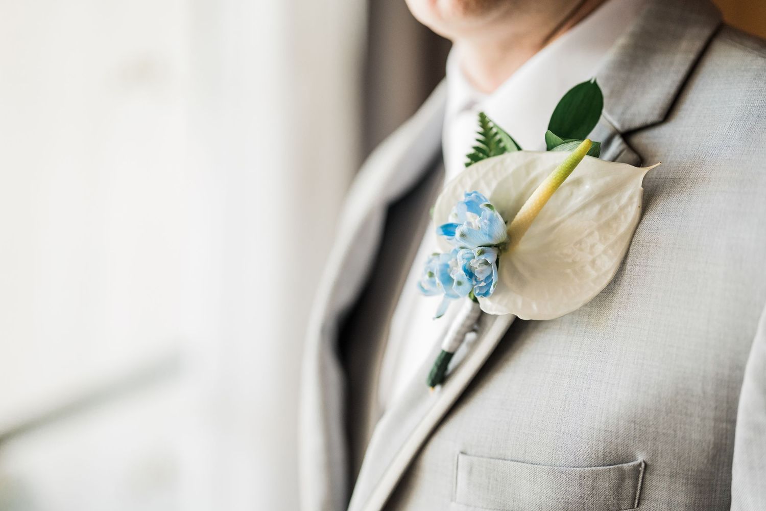 Close-up of a groom's gray suit lapel with a white calla lily and blue floral boutonniere.