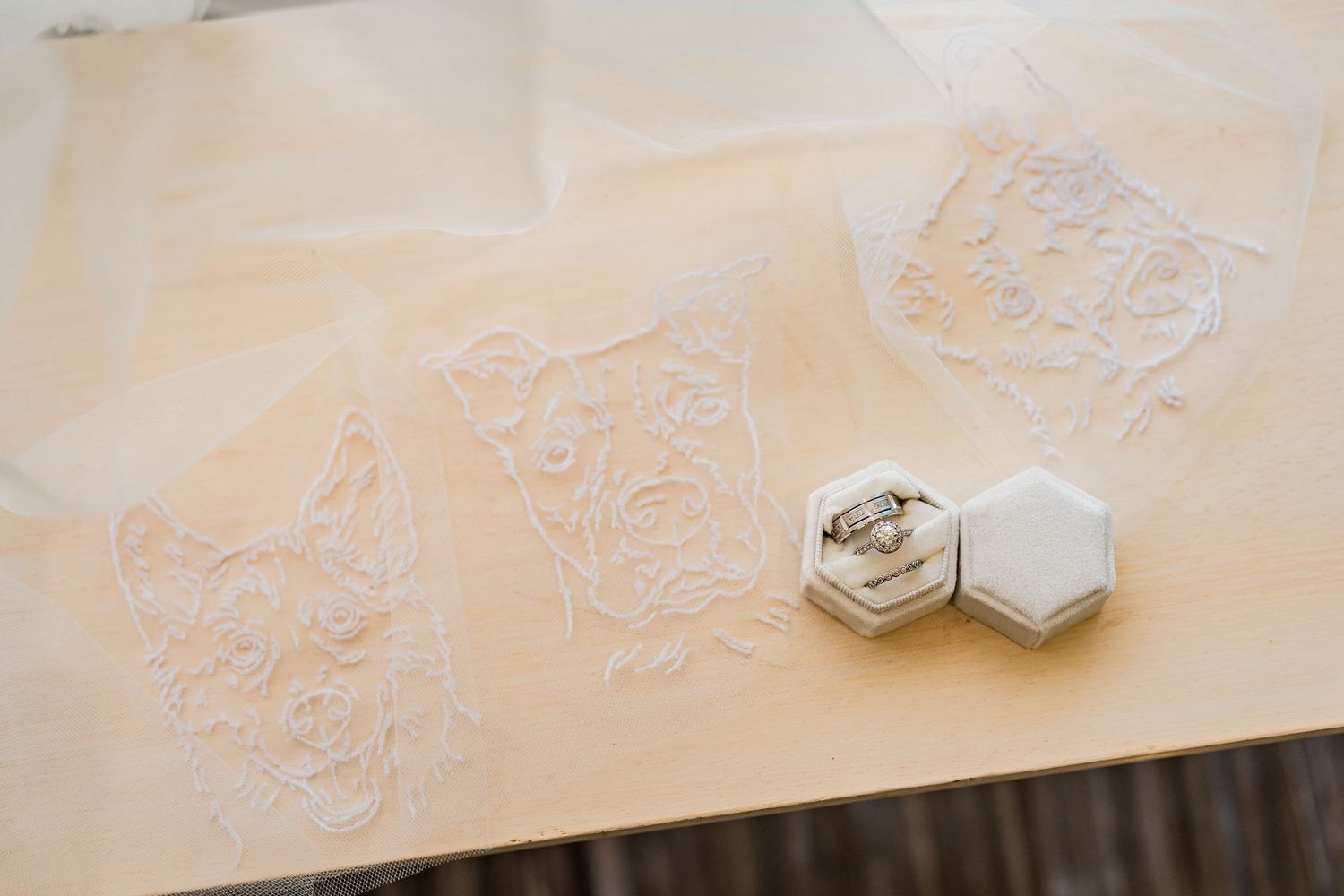 Elegant wedding rings displayed in a white hexagonal velvet box beside delicate lace fabric pieces on a wooden surface.