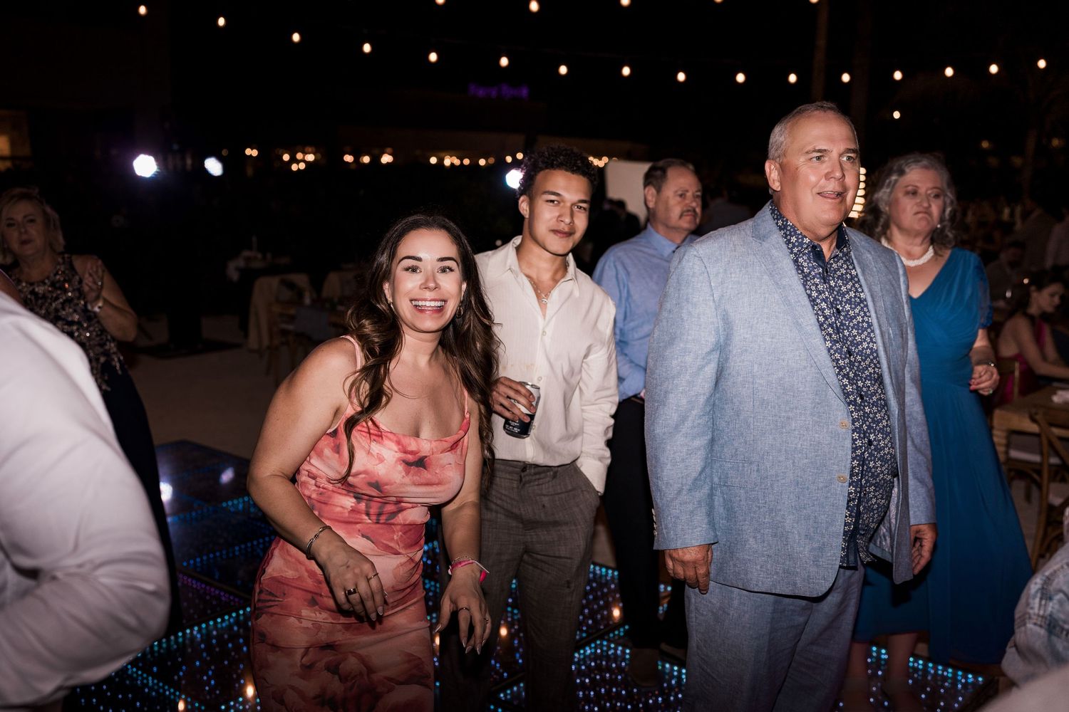 Three guests smiling and posing together on a dance floor at an elegant outdoor evening wedding reception.