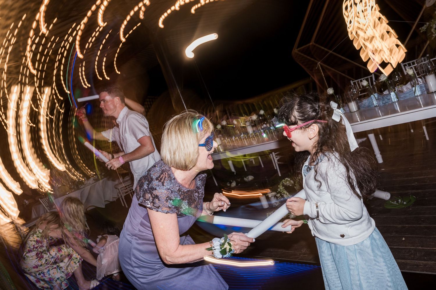 Woman bends down to interact with a child wearing a red nose at a festive party with glowing lights.