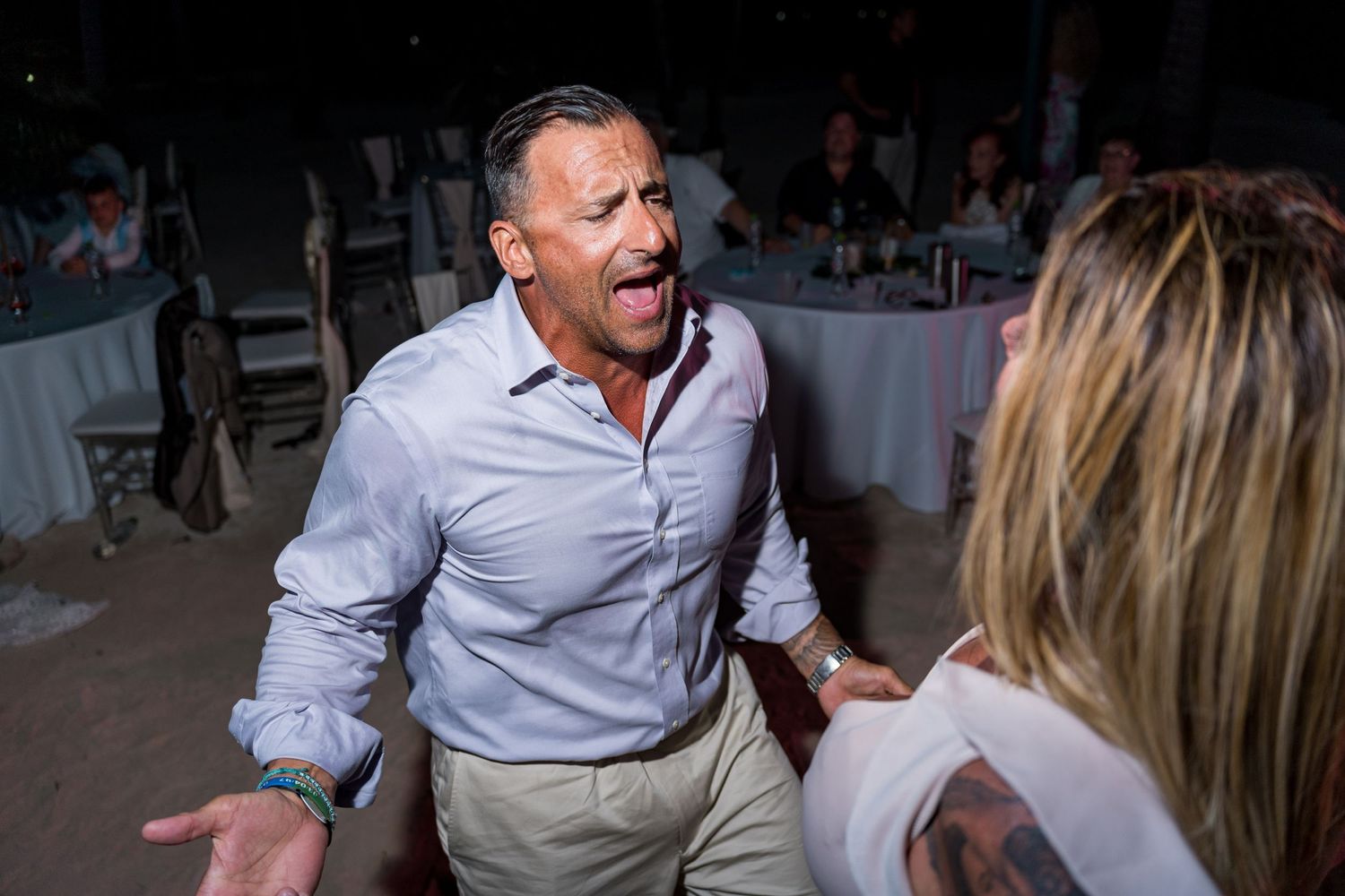 Excited man in white shirt celebrating enthusiastically at an outdoor beach wedding reception.