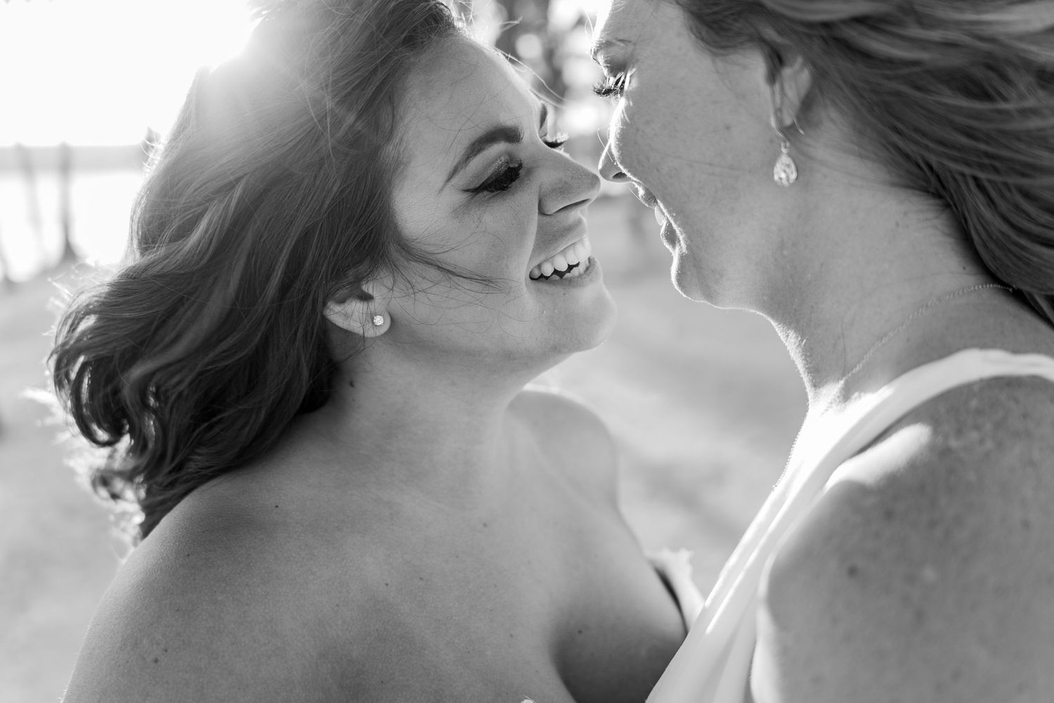 Black and white close-up of two women smiling intimately at each other during a wedding.