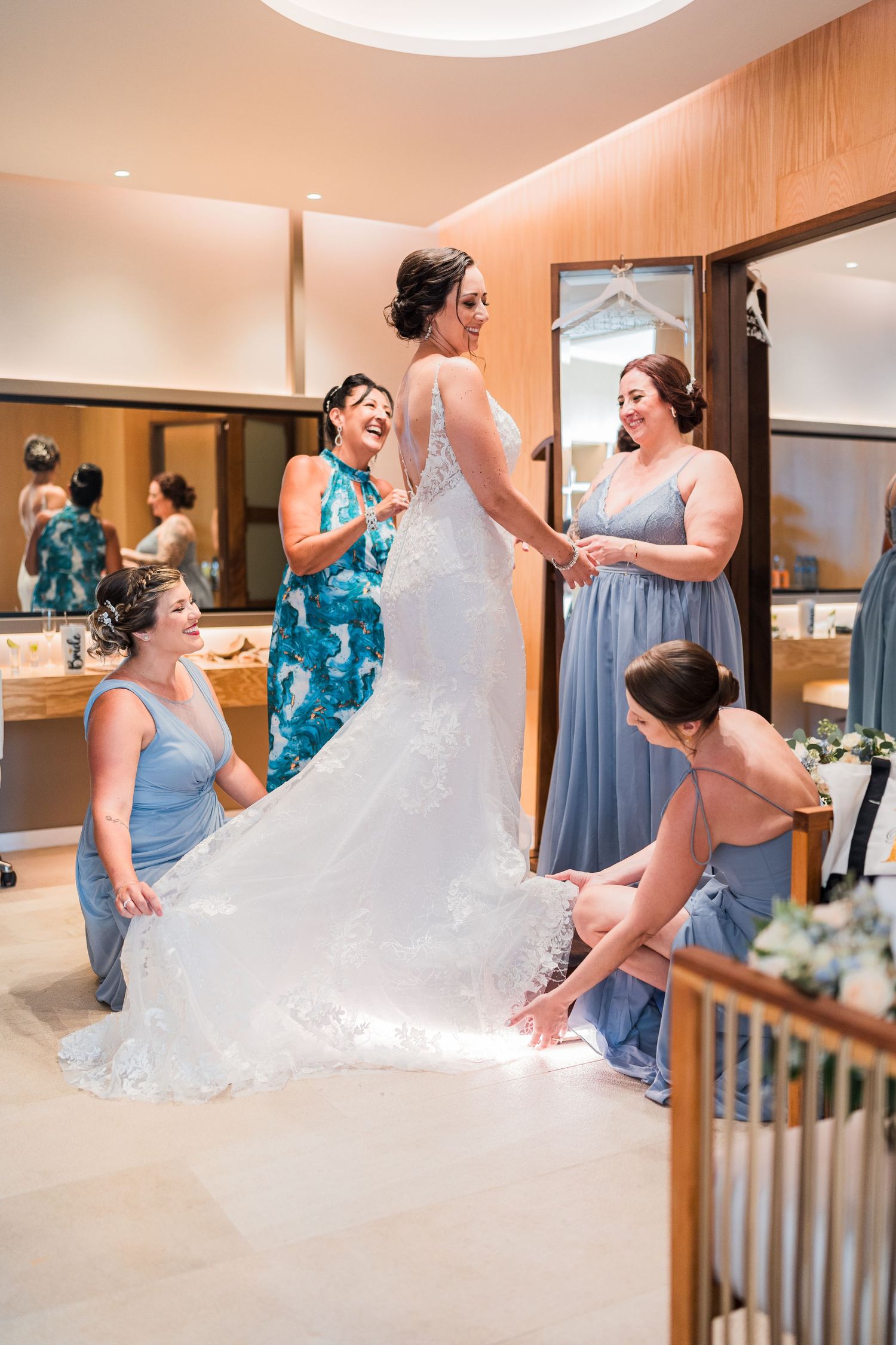 Bridesmaids in blue dresses helping bride get ready in modern hotel suite.