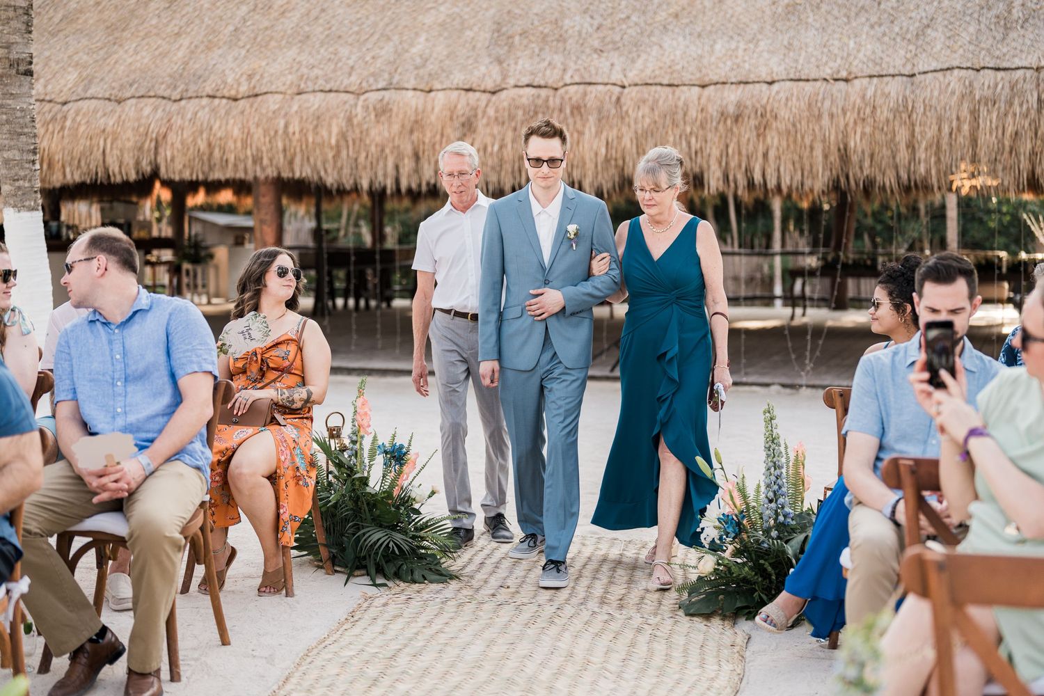 Groom escorted down the aisle by his parents at a tropical beach wedding ceremony.