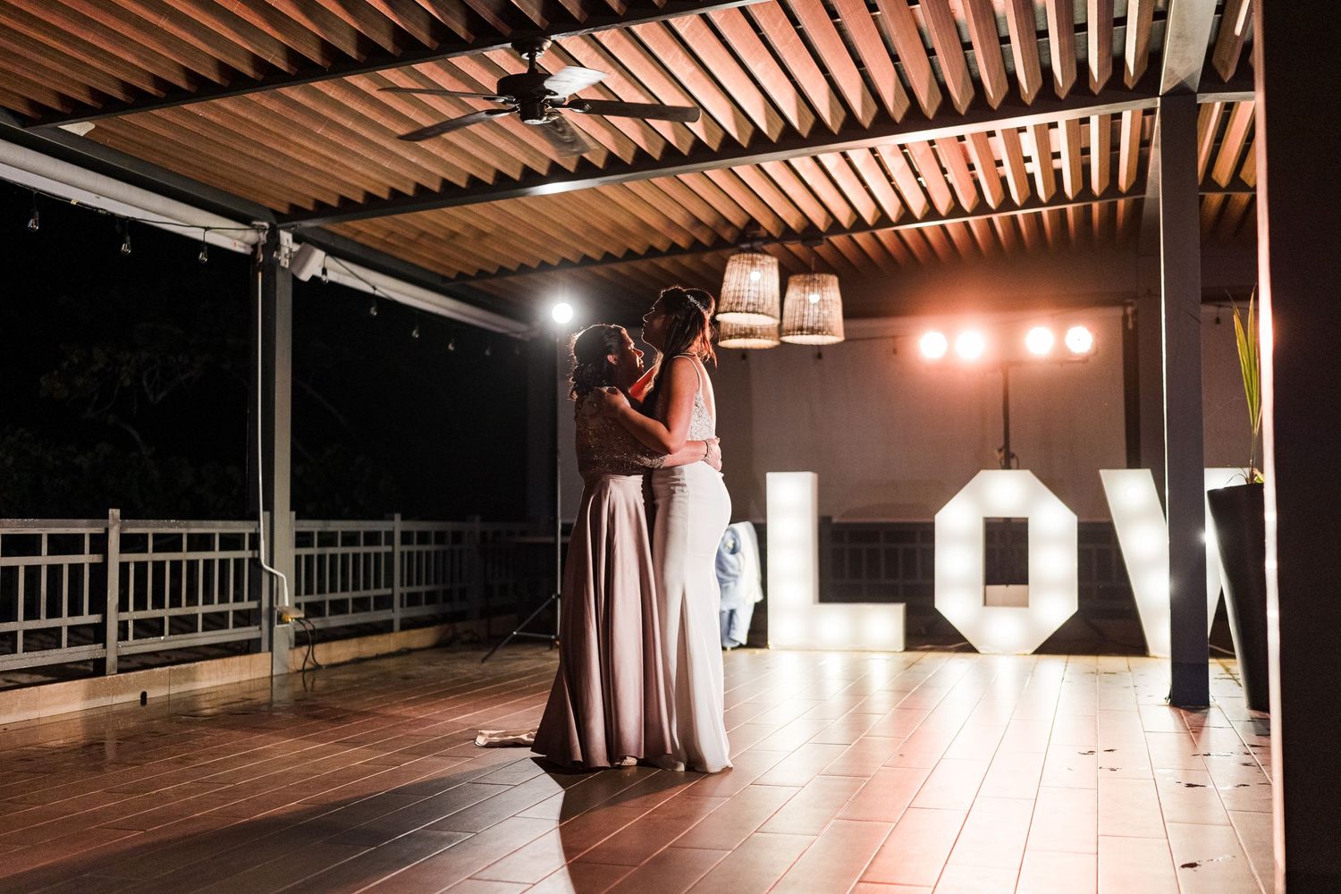 Couple sharing a romantic slow dance in front of glowing LOVE marquee letters at night reception.