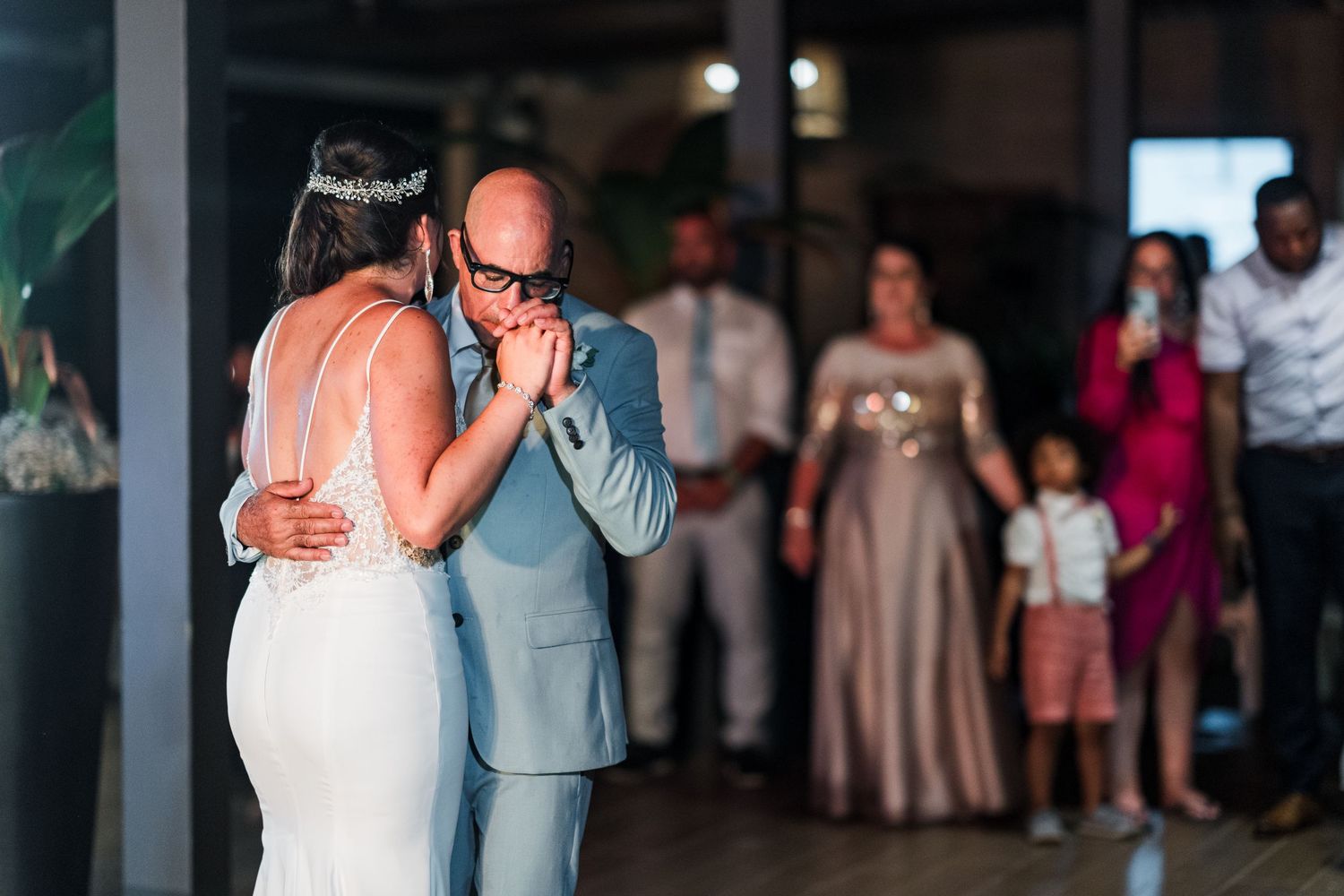 Bride and groom share first dance as wedding guests watch lovingly during outdoor reception celebration.