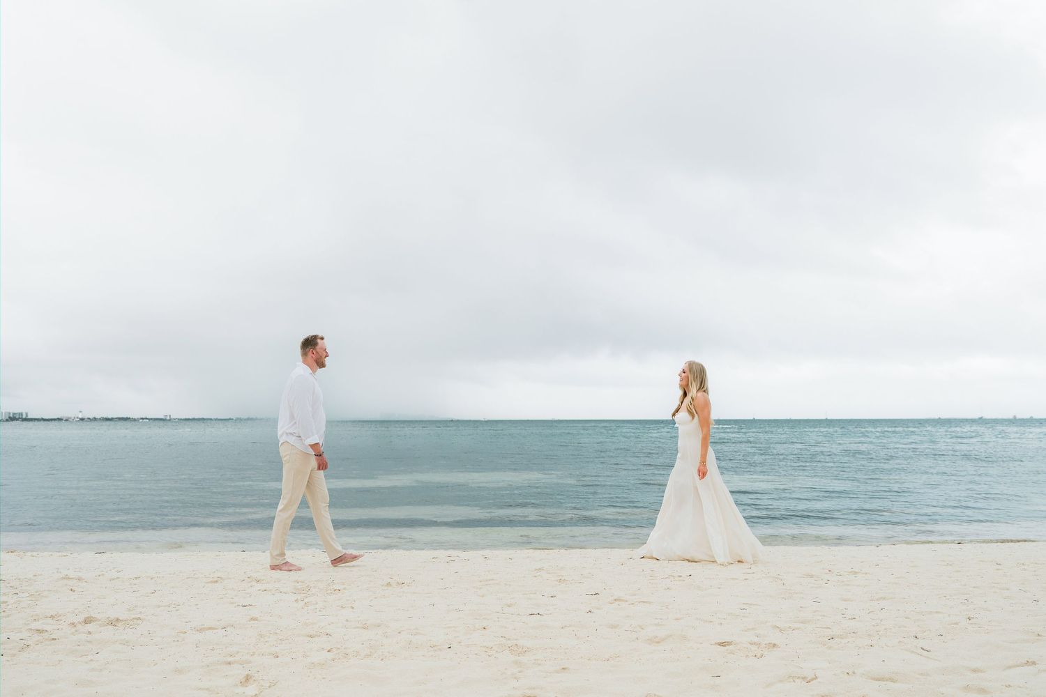 Cancun Engagement Photoshoot - Bride and groom walking on a white sandy beach with calm ocean waters and overcast skies