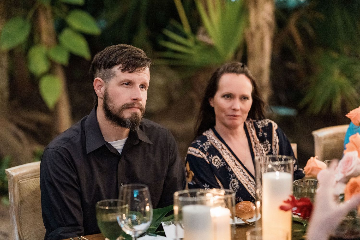 Secrets Akumal Wedding - A man with a beard and a woman in a patterned top sit at an elegant outdoor dinner table with candles.